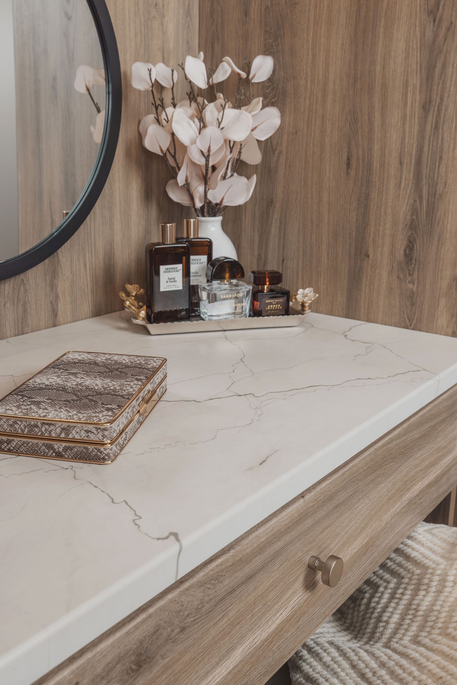 Bedroom dresser with white marble top, woven tray, perfume bottles, and dried flowers against wood-paneled wall
