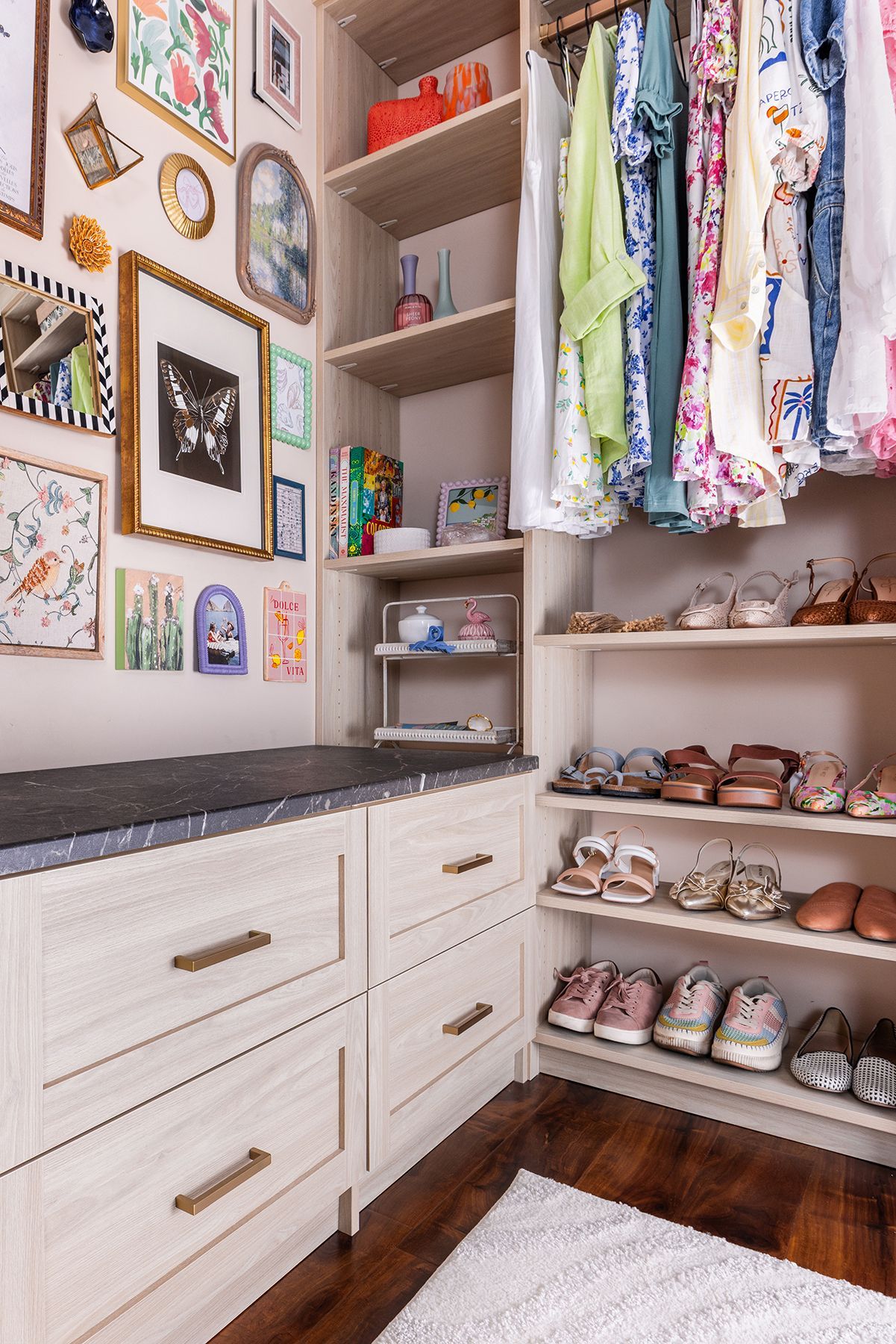 Bright walk-in closet with white drawers, hanging clothes, shelves of shoes, and framed wall art.