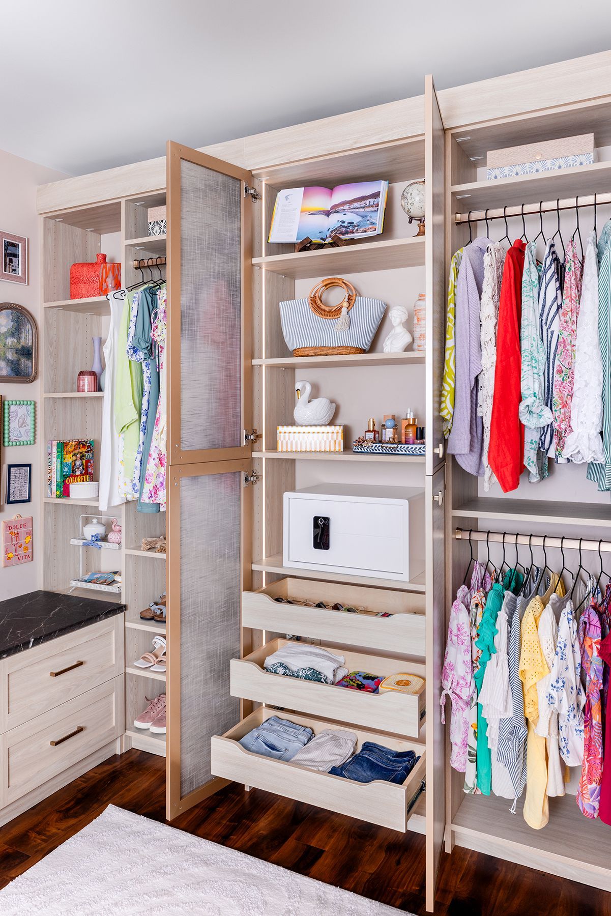 Open closet with wood shelves, hanging clothes, drawers, and storage bins in a bright bedroom.