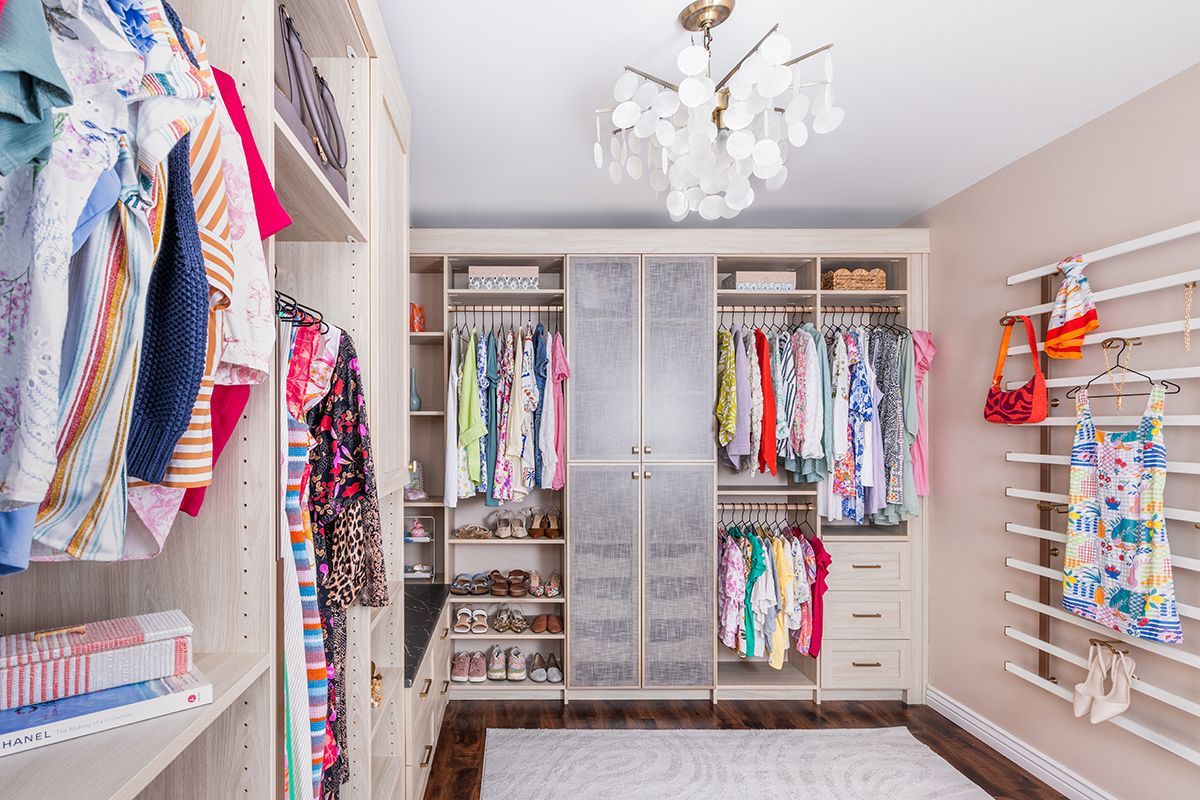 Bright walk-in closet with hanging clothes, built-in shelves, and a chandelier