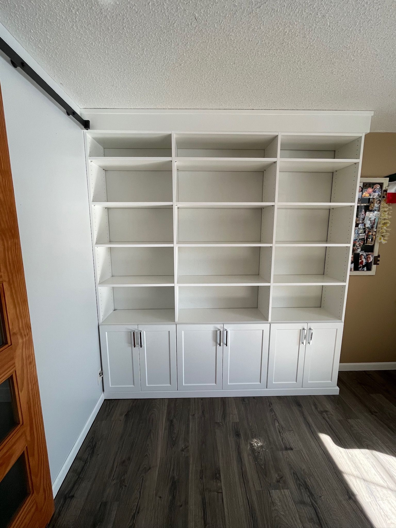 White built-in shelving and cabinets against a wall in a room with dark wood flooring.
