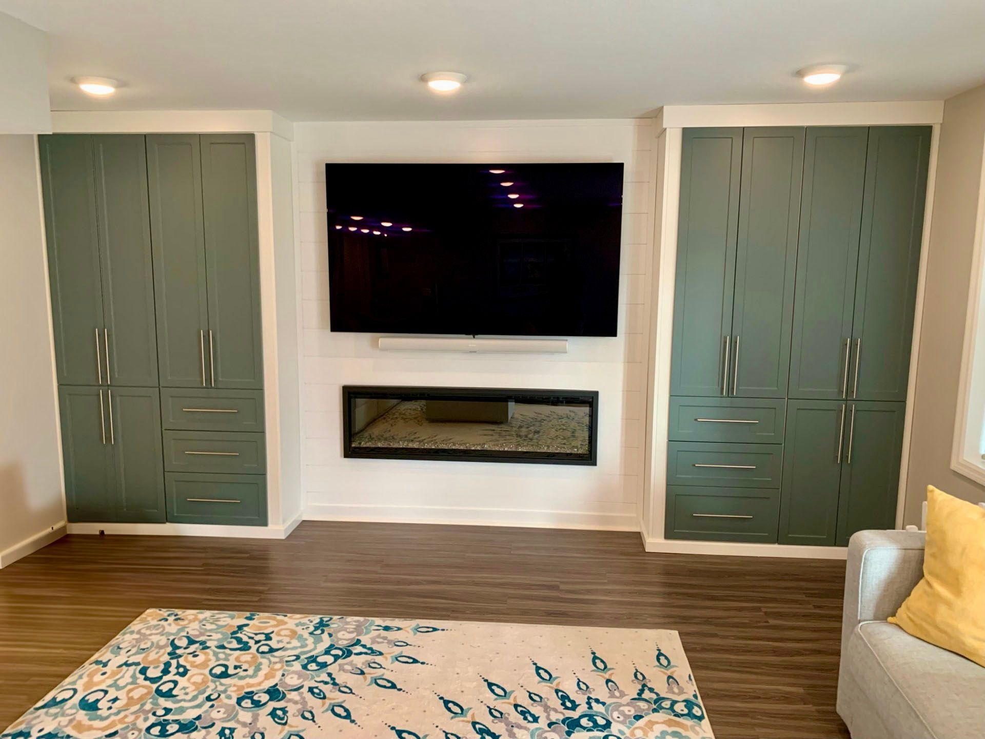 Modern living room with wall-mounted TV, fireplace, teal cabinets, wood floor, and patterned rug.