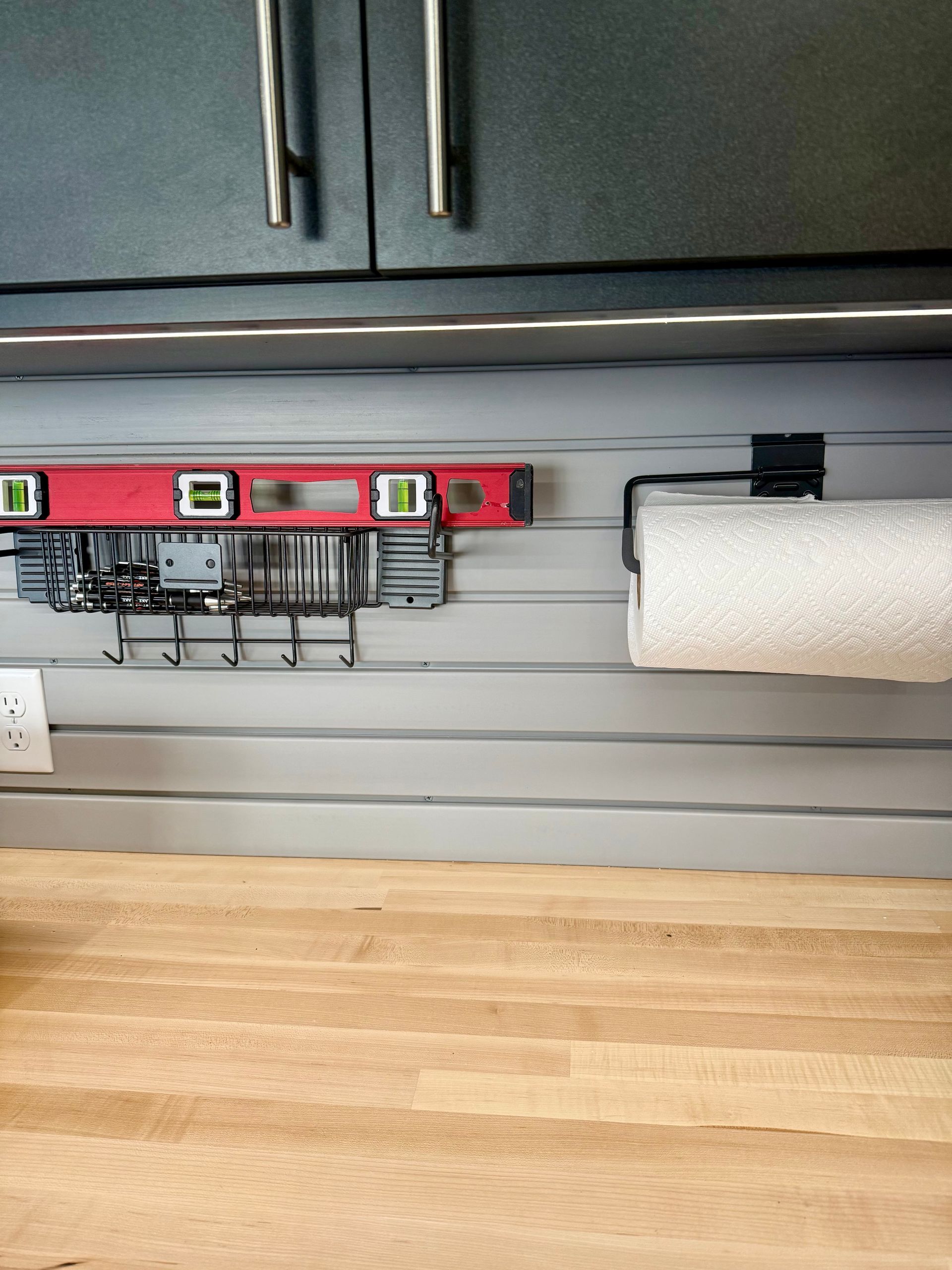 Under-cabinet mounting setup with a red level, hanging cable organizer, and paper towel roll in a kitchen.