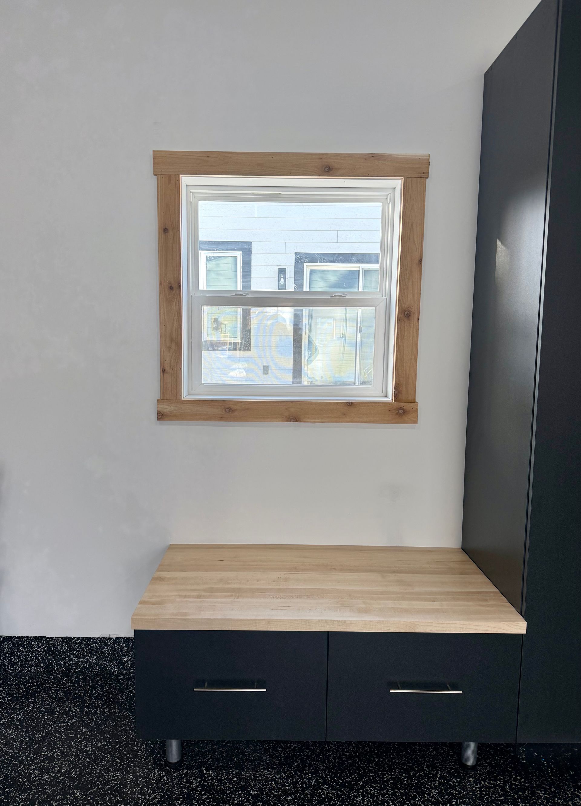 Small wooden bench with dark drawers beneath a window in a light-colored room.