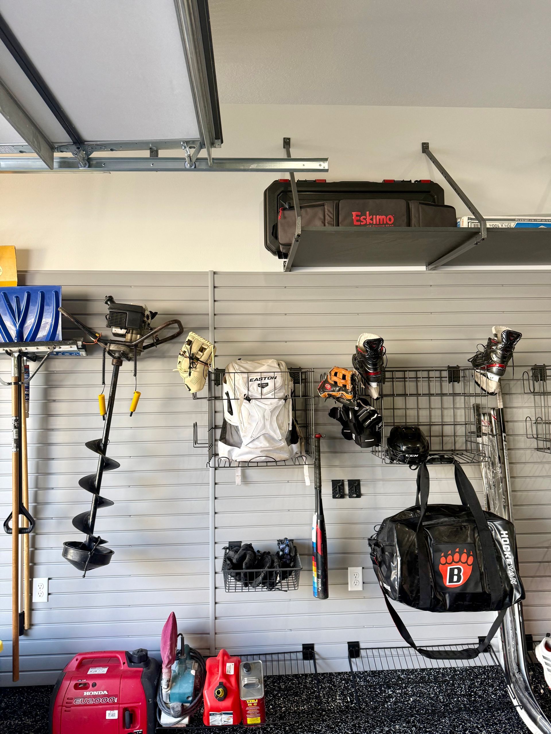 Garage wall with hanging tools, equipment, and a red snowblower beneath an overhead garage door opener