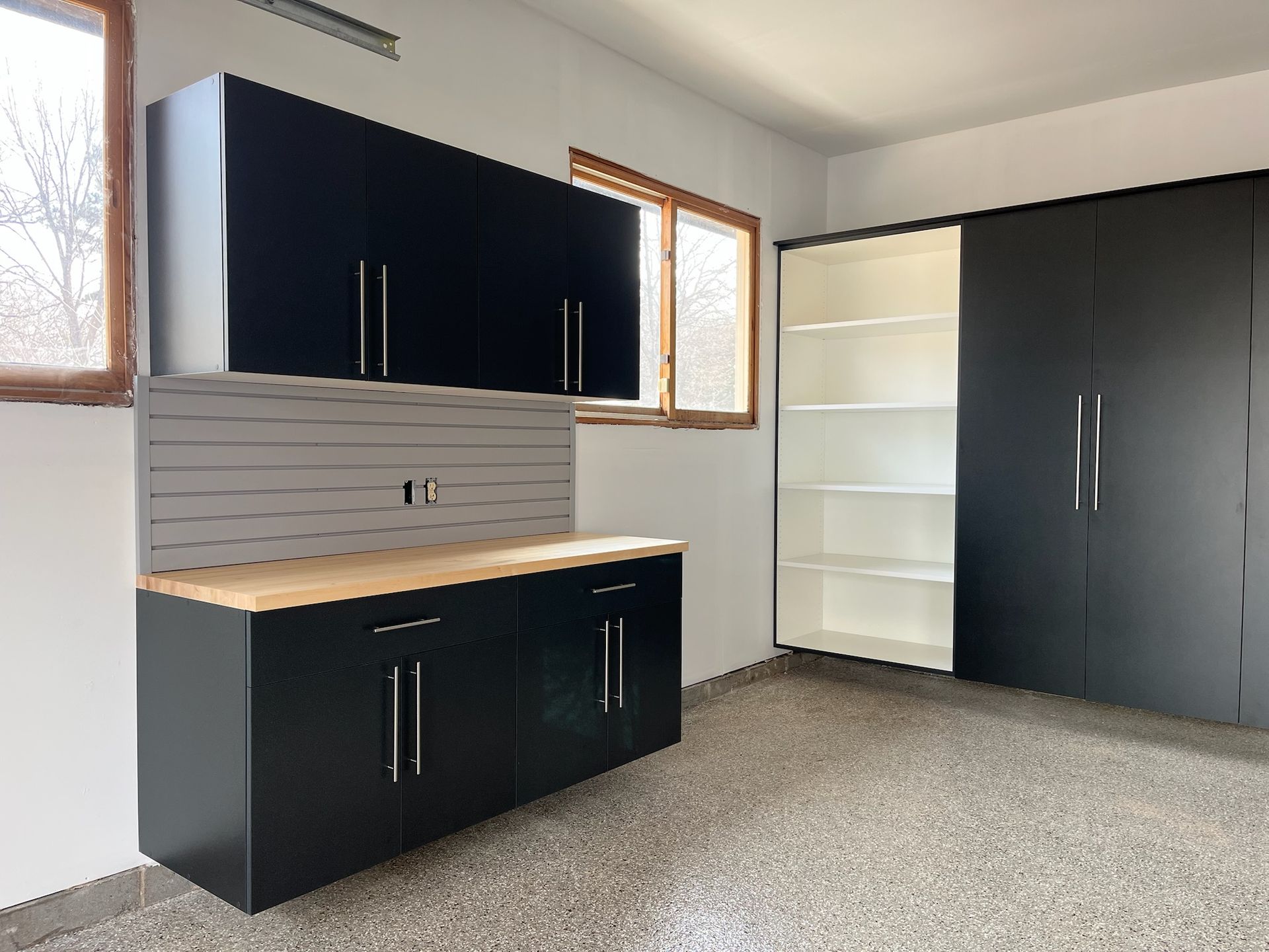 Modern kitchen with black cabinets, light wood countertop, and white shelving in a gray room