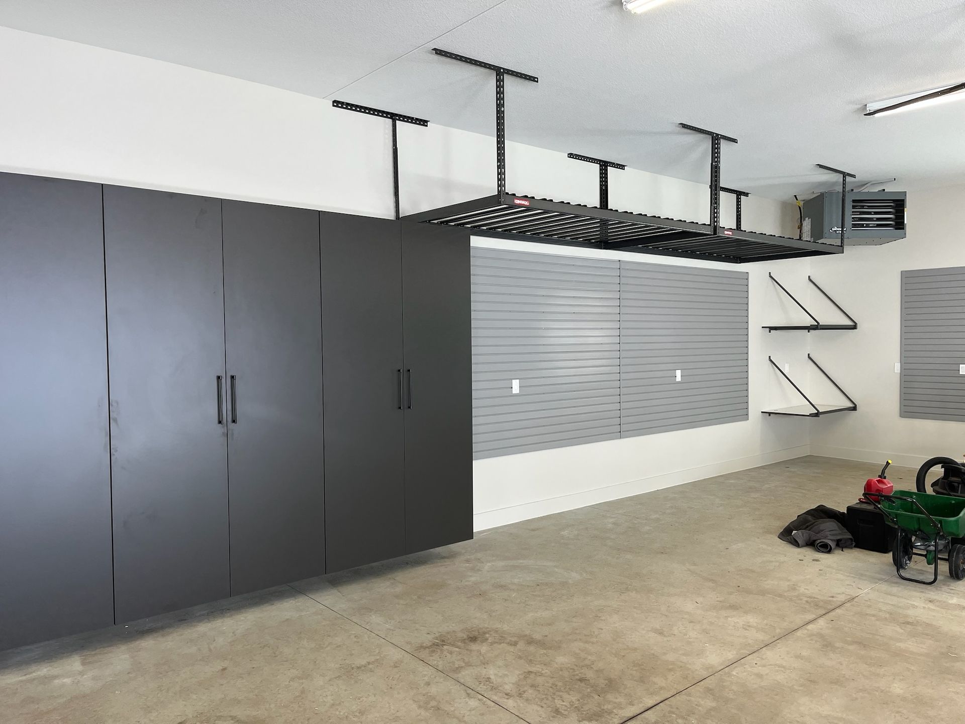Garage with dark cabinets, wall-mounted storage, and items on the concrete floor.