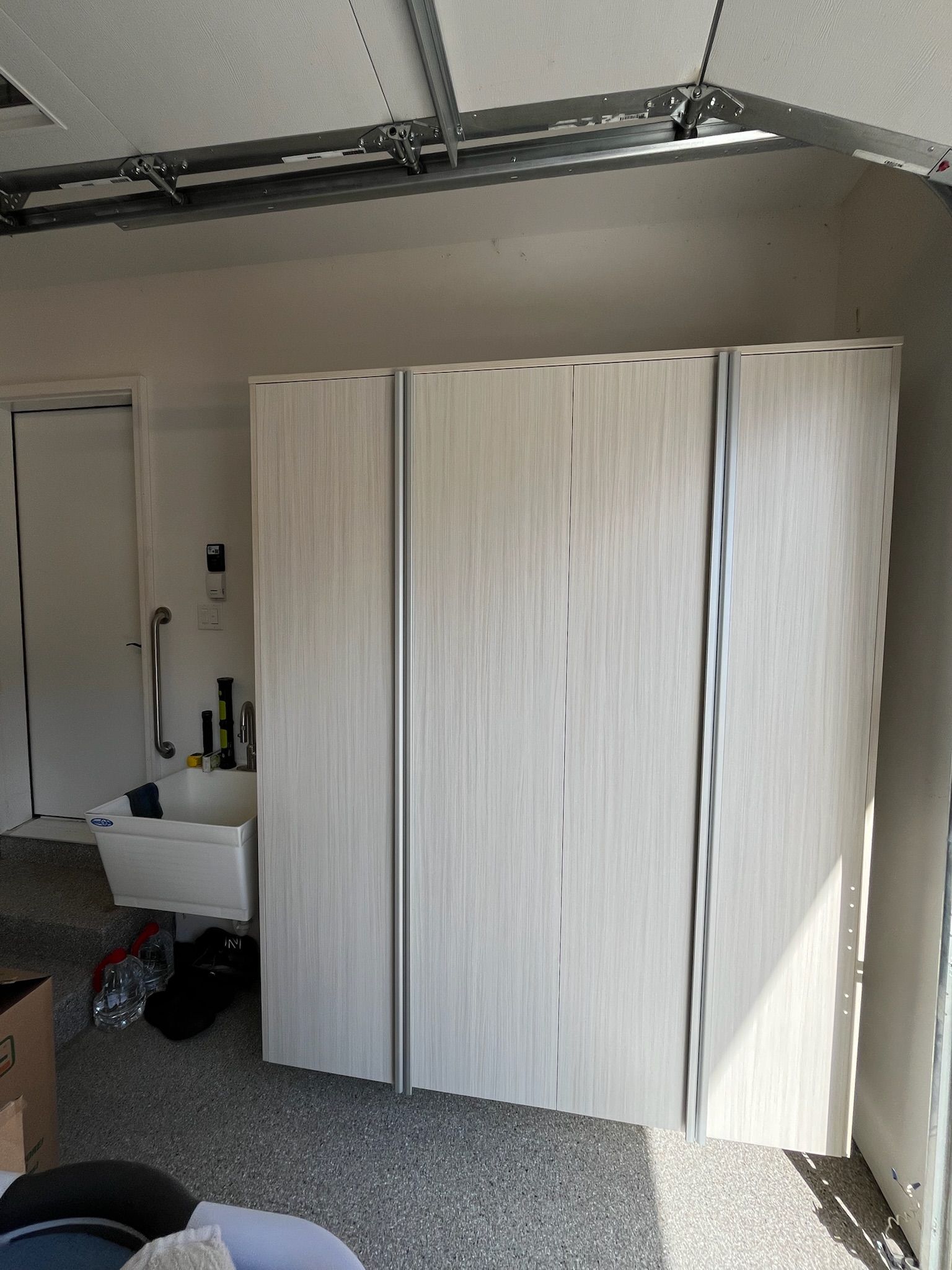 Three white wardrobe panels in a garage, with a white utility sink and ceiling track lights visible.