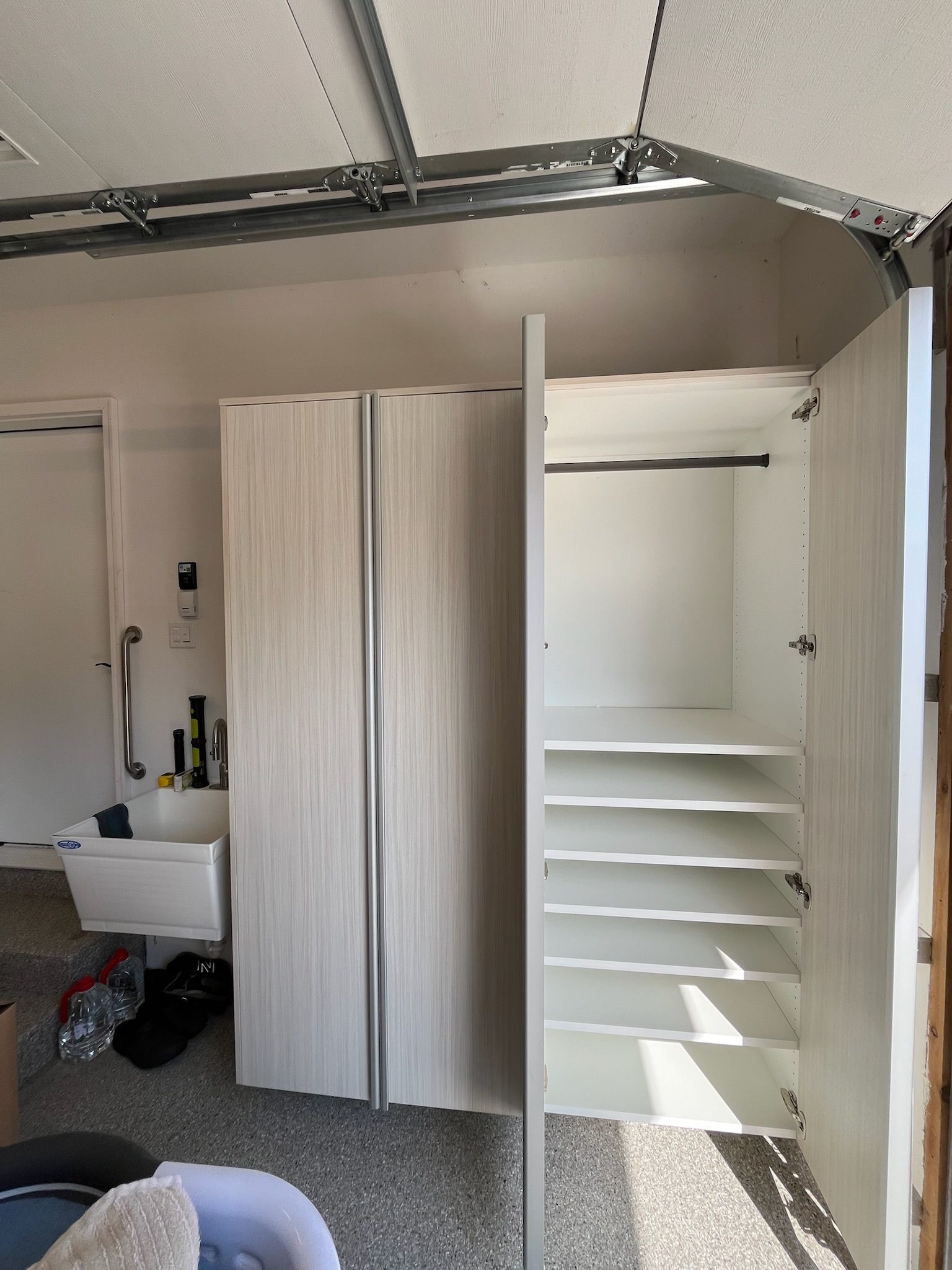 Open garage storage cabinets with shelves, a sink, and garage door tracks visible overhead.