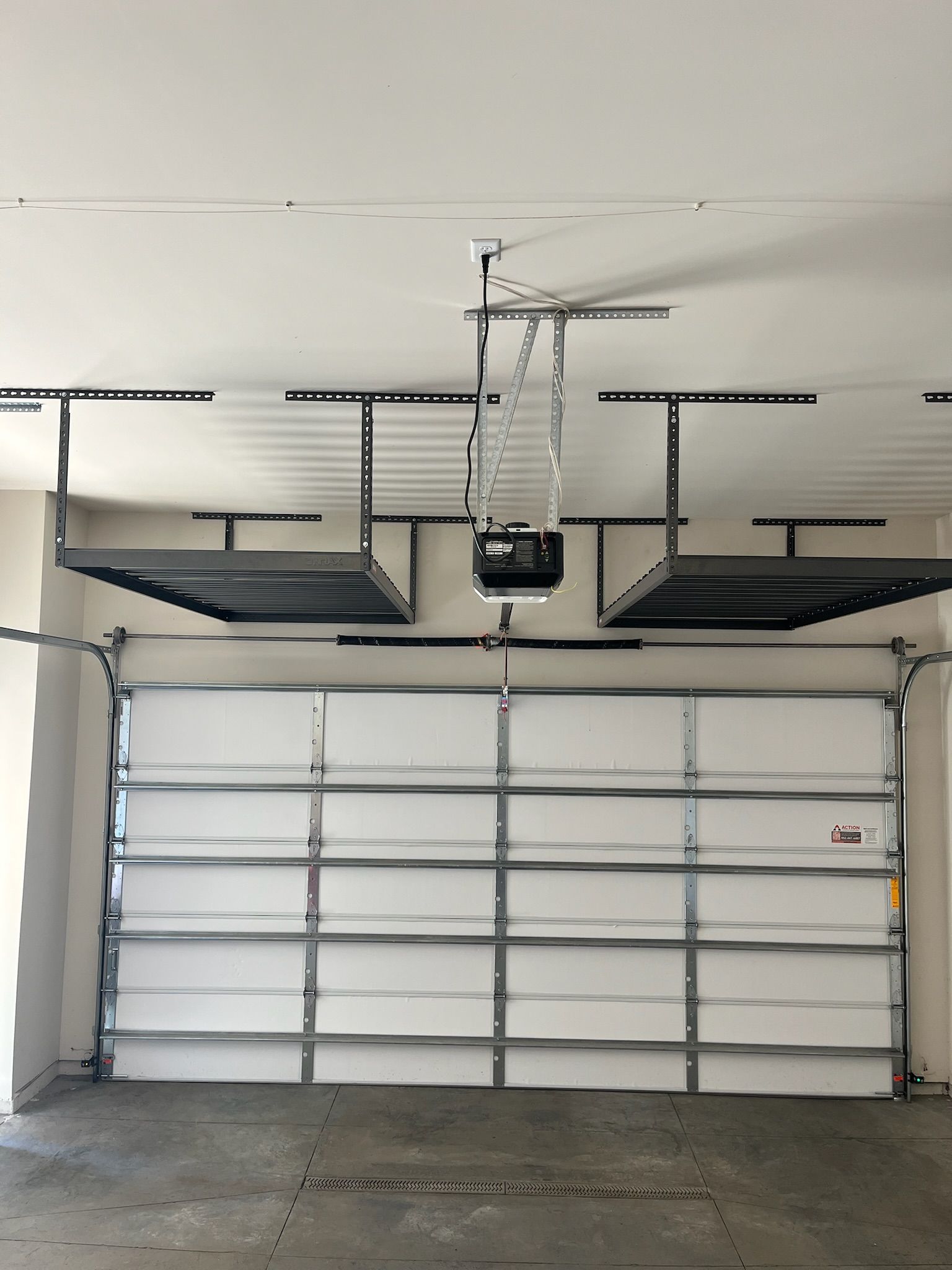 Two white garage doors with an overhead garage door opener in a plain garage interior.