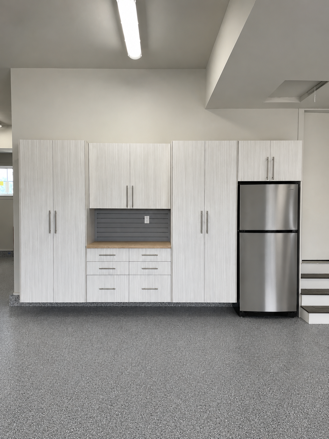 Modern break room with white cabinets, stainless steel fridge, and gray speckled floor.