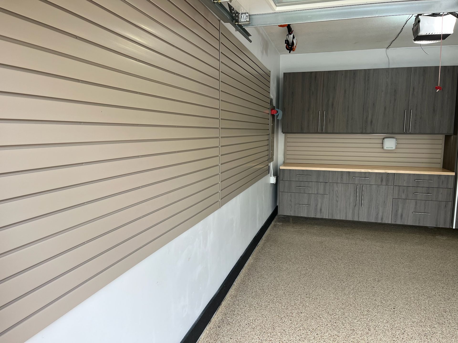 Empty garage interior with beige slat wall, white lower wall, gray cabinets, and speckled floor.