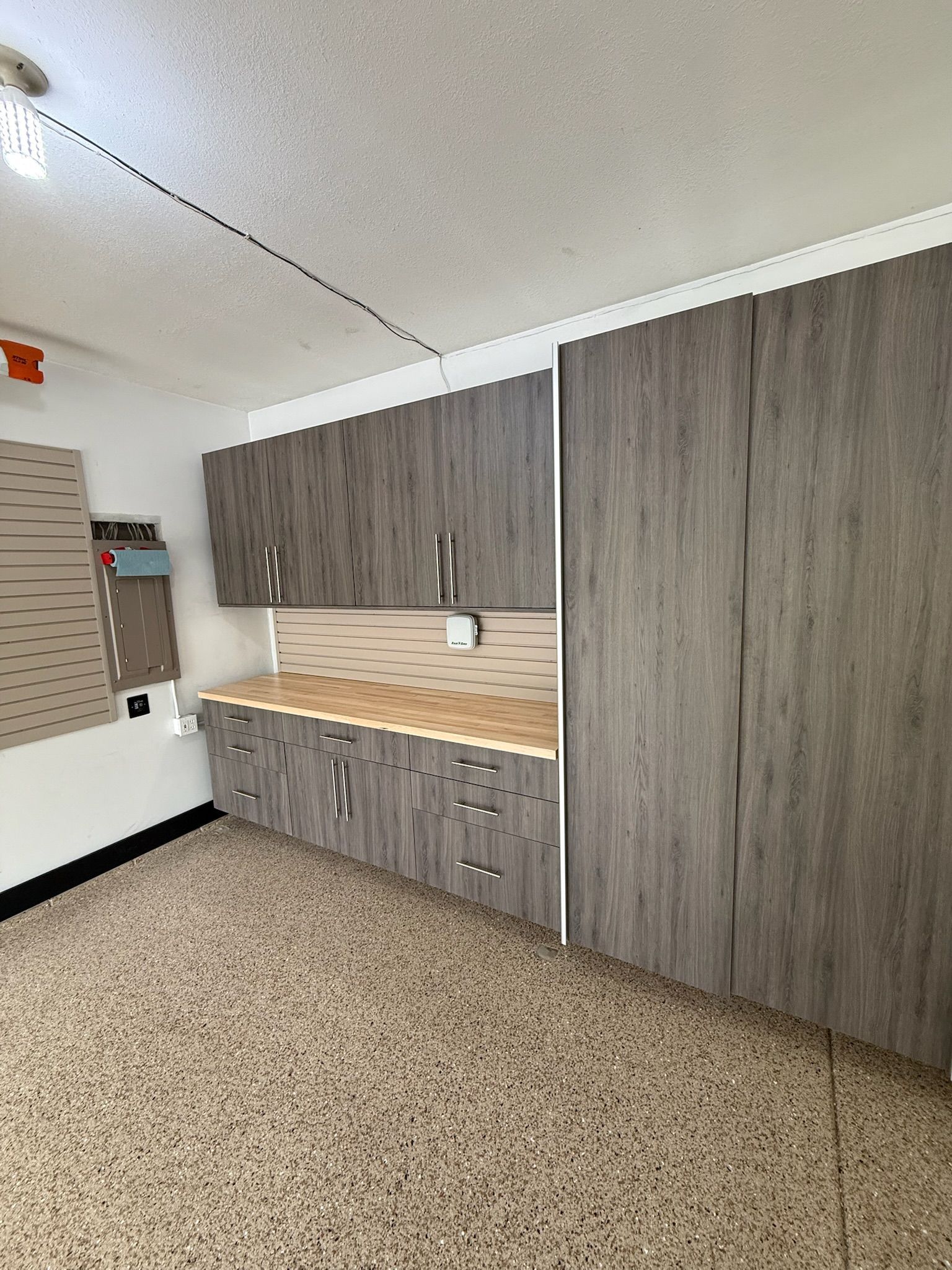 Small kitchenette with gray cabinets, wood countertop, sink, and beige speckled flooring in a room.
