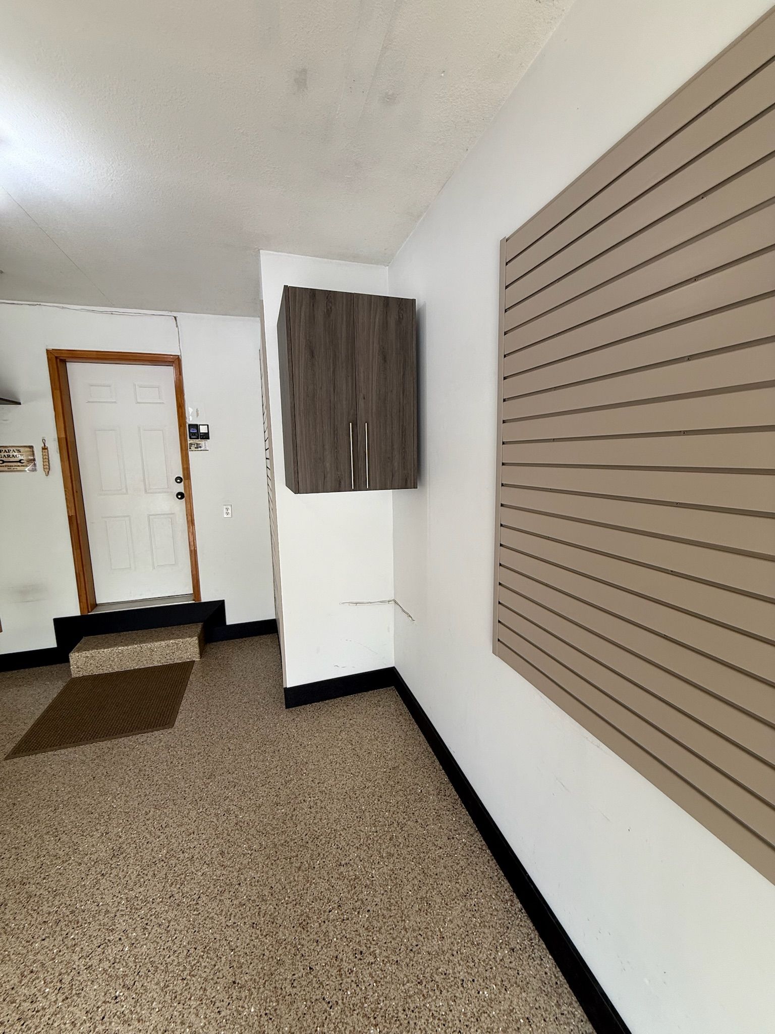 Empty room with white walls, brown carpet, a door, and a large slat wall panel.
