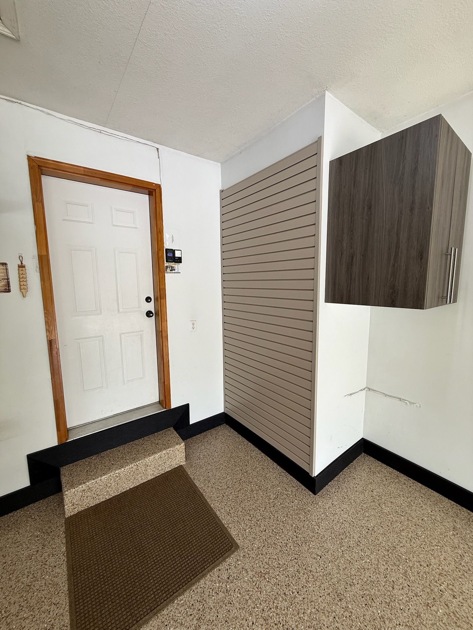 Apartment entryway with white door, wood trim, beige walls, and a built-in cabinet next to a pegboard wall.