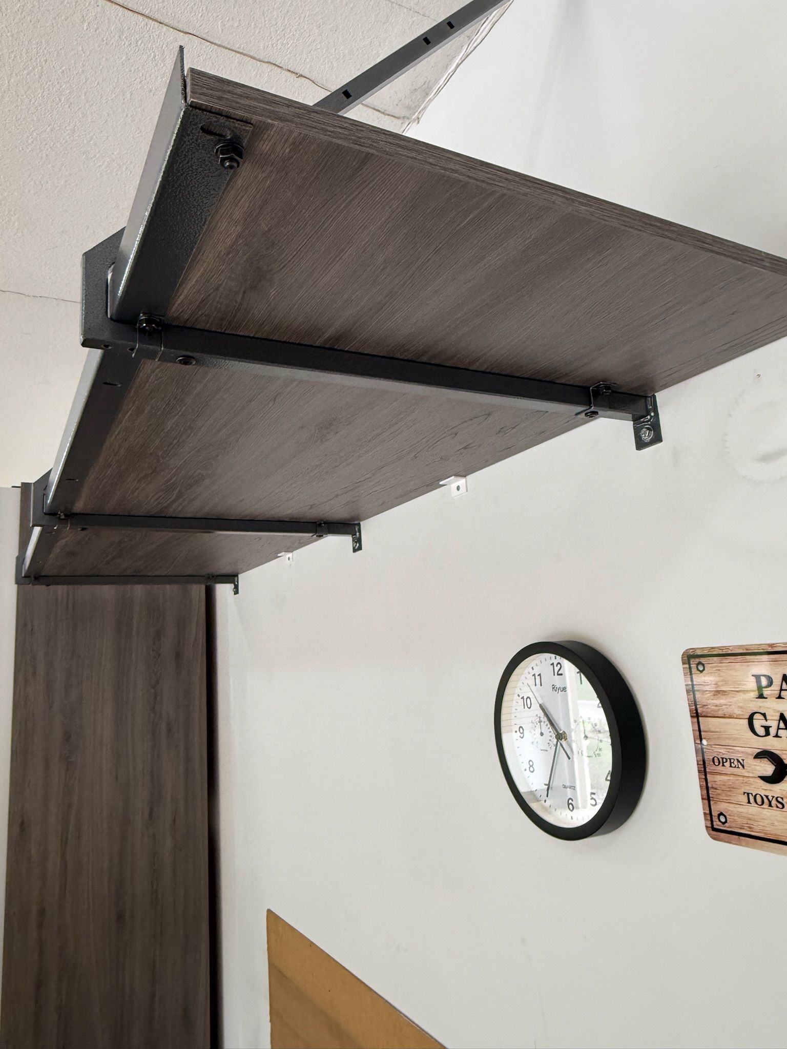 Wall-mounted black shelf above a white wall with a clock and sign below