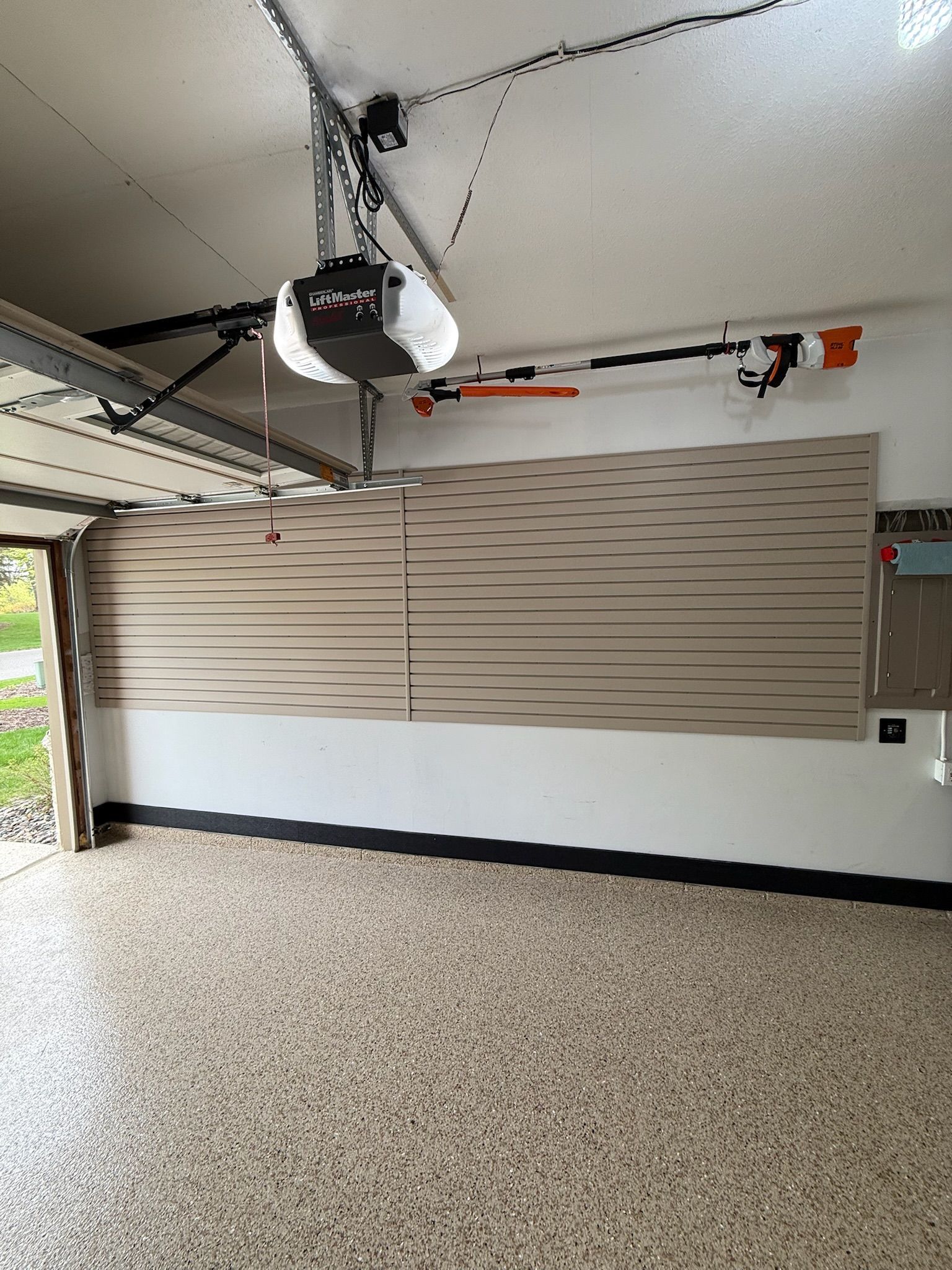 Interior of a garage with a closed beige panel garage door and a ceiling-mounted opener.
