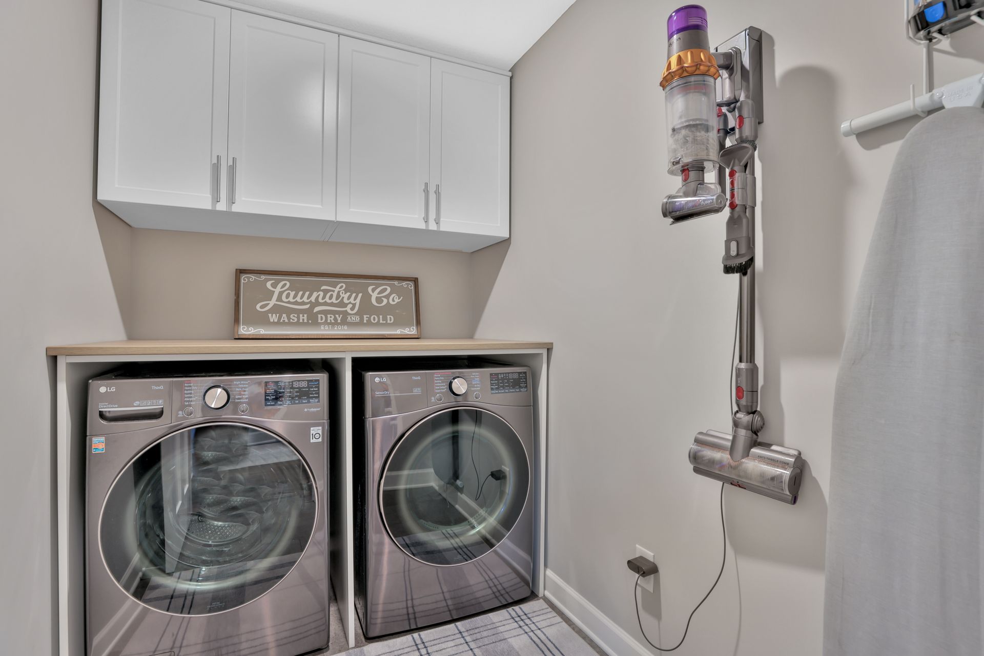 Laundry room with front-load washer and dryer, white cabinets, and exposed plumbing on the right