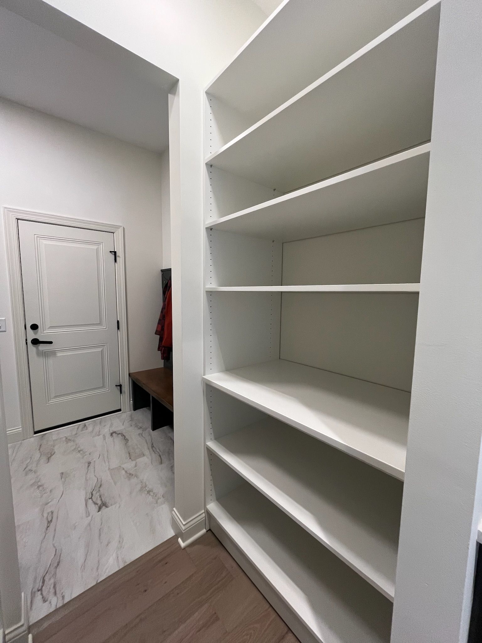 Narrow walk-in closet with white shelves and a white door, viewed from the doorway.