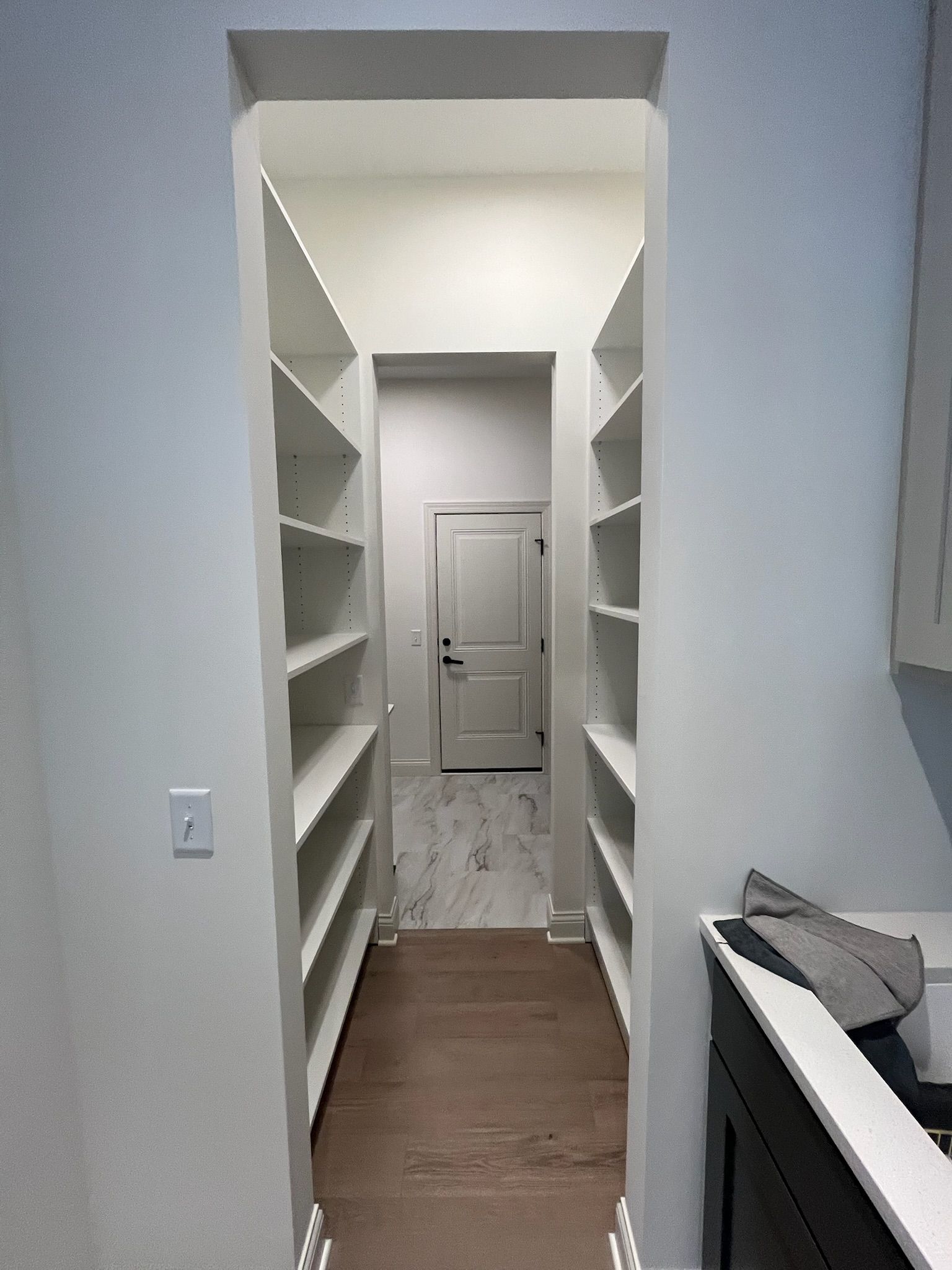 Narrow white closet hallway with built-in shelves leading to a closed door at the end