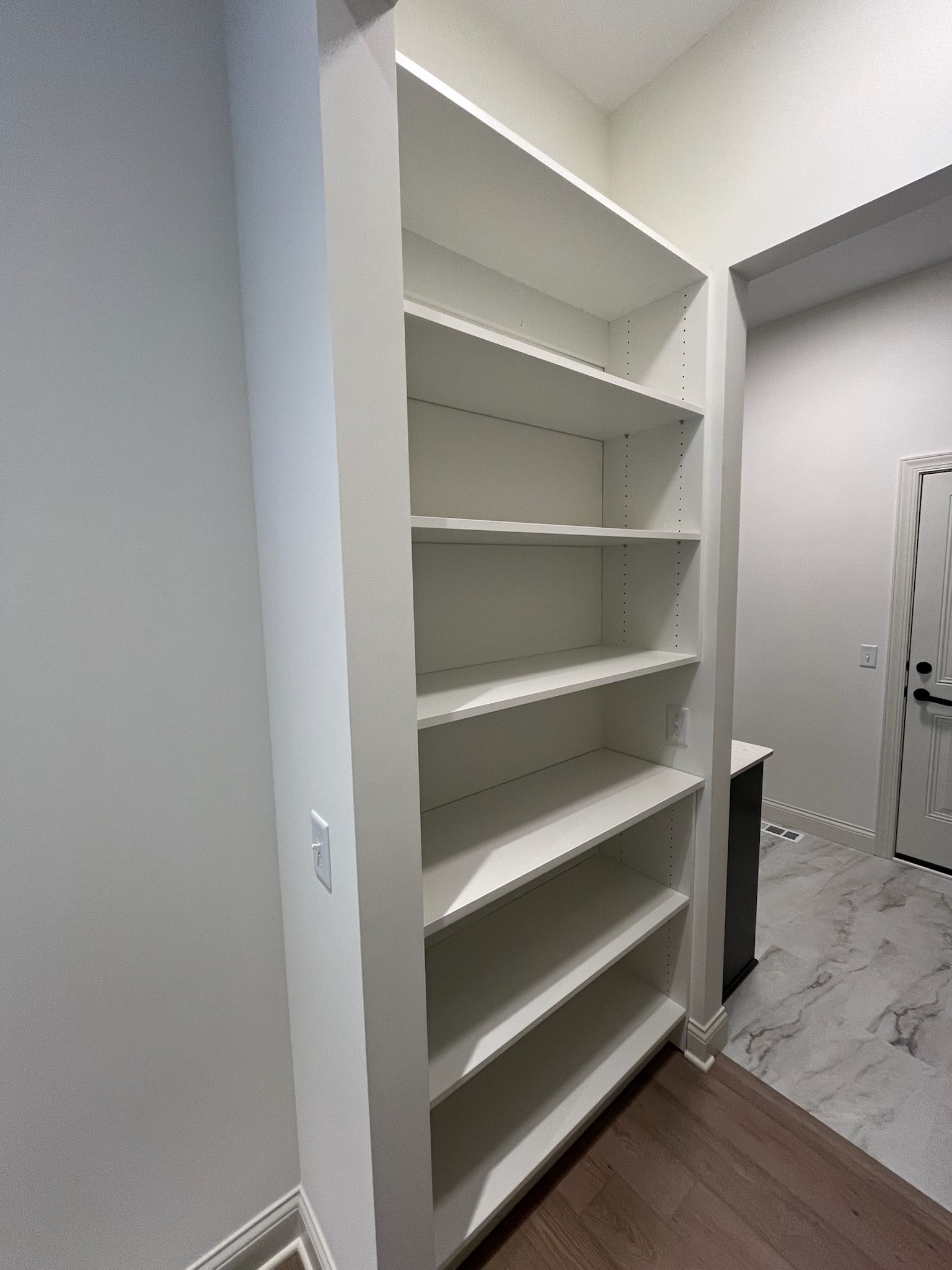 Built-in white shelving in a hallway with gray walls and marble-patterned flooring.