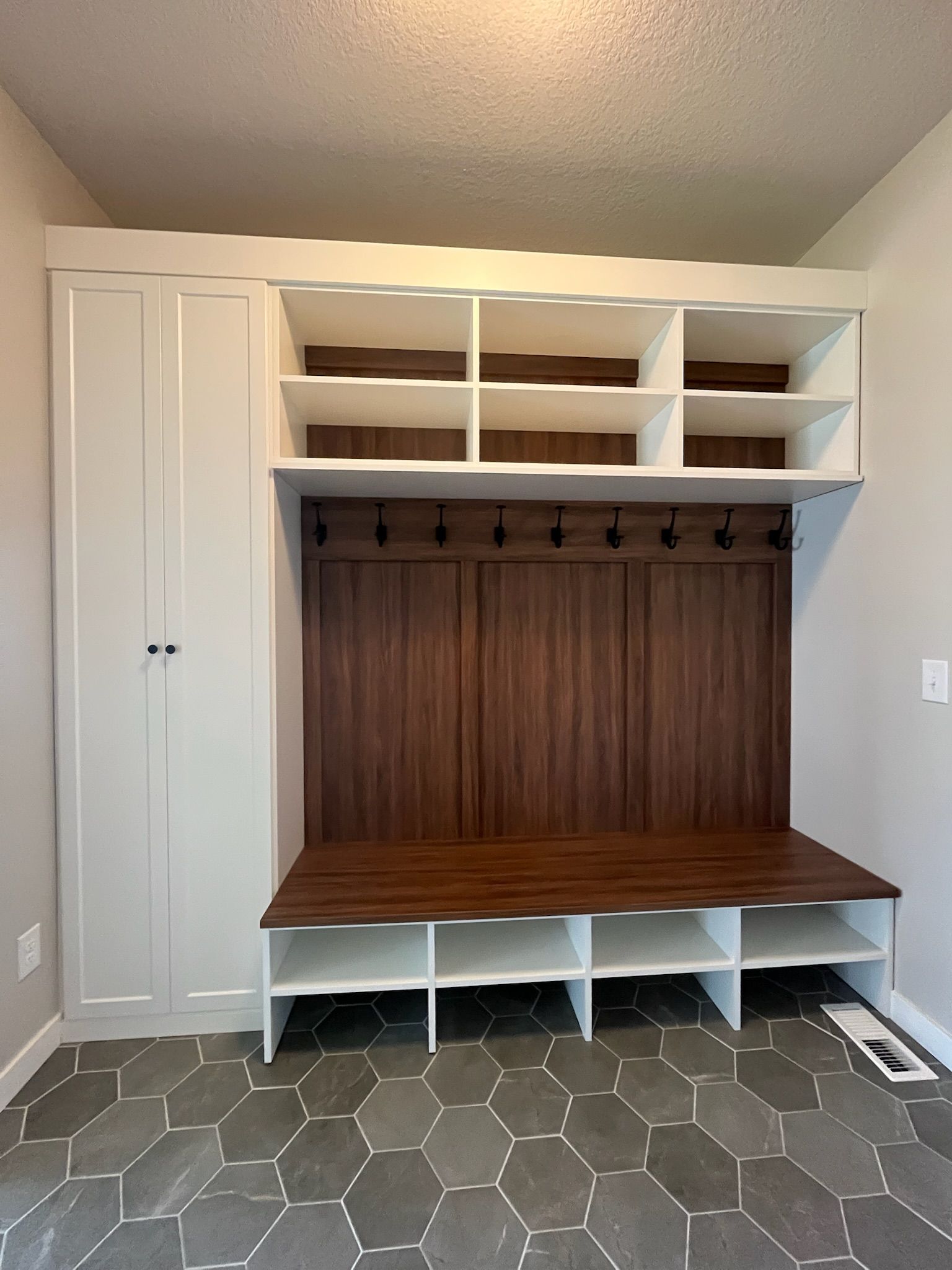Built-in white mudroom bench with wood back panel, cubbies, and upper storage shelves in a room with hex tile floor