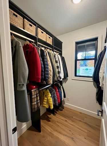 Walk-in closet with hanging coats, storage baskets, and a window on the right