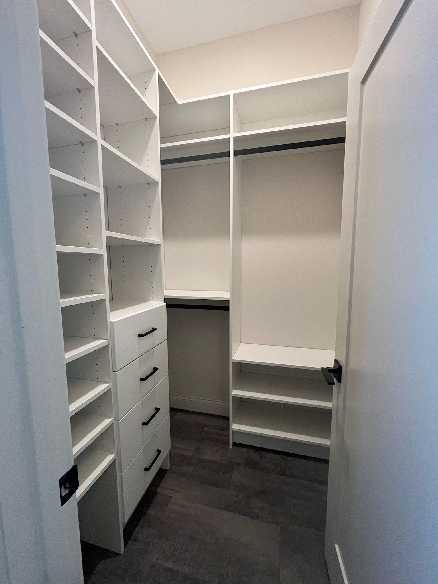 Empty white walk-in closet with built-in shelves, drawers, hanging rods, and dark wood flooring.
