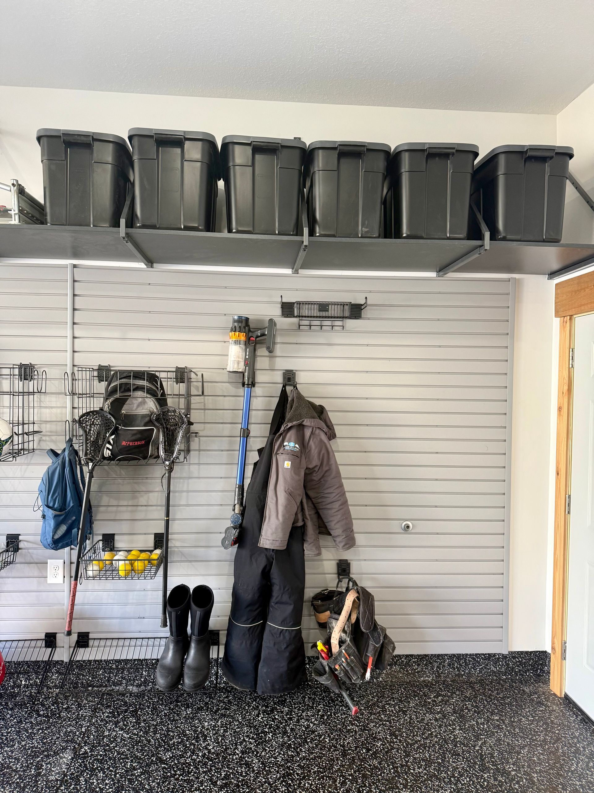 Garage wall with coat hooks, rain boots, bike gear, and storage bins on overhead shelves.