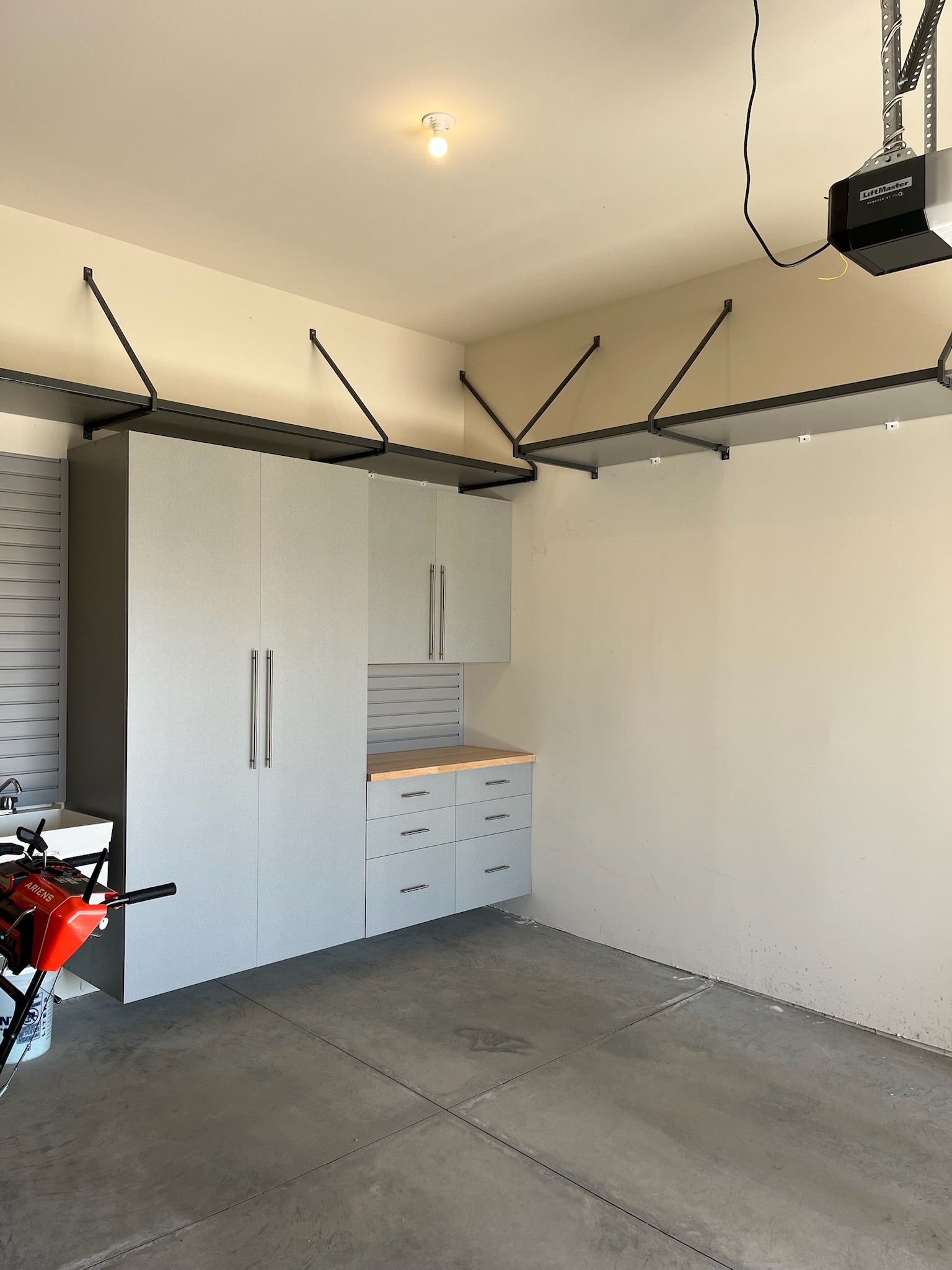 Garage with open cabinets, a workbench, wall-mounted storage, and a motorcycle at left.