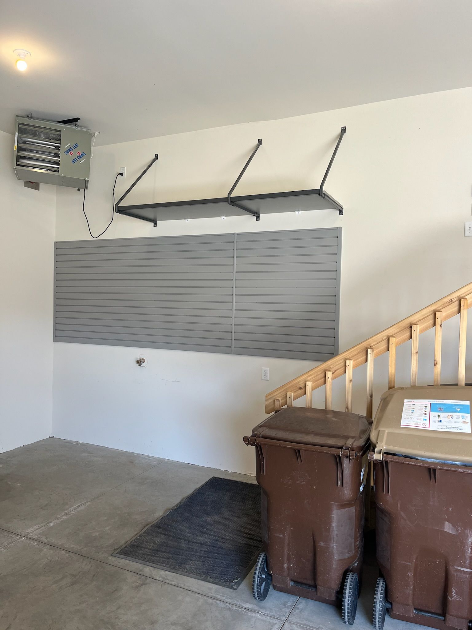 Garage interior with wall-mounted storage, a barred window, and two brown trash bins by stairs
