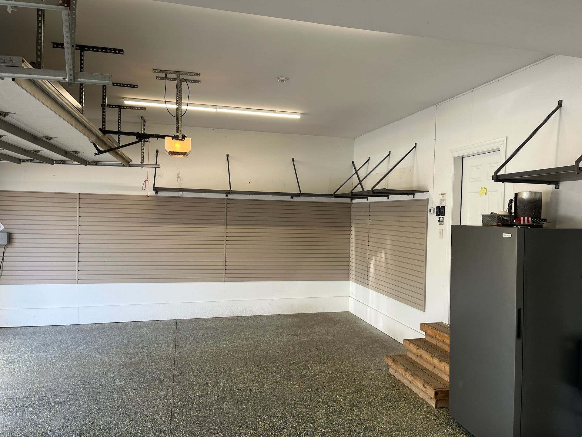Empty garage with closed beige door, gray floor, wall cabinet, and stacked boxes on the right