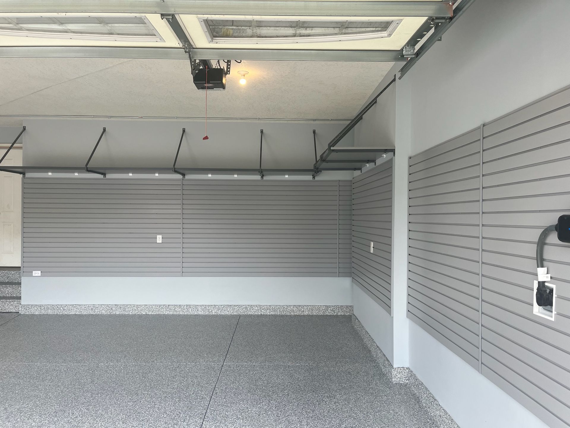 Empty garage interior with gray roll-up door, white walls, and speckled epoxy floor.