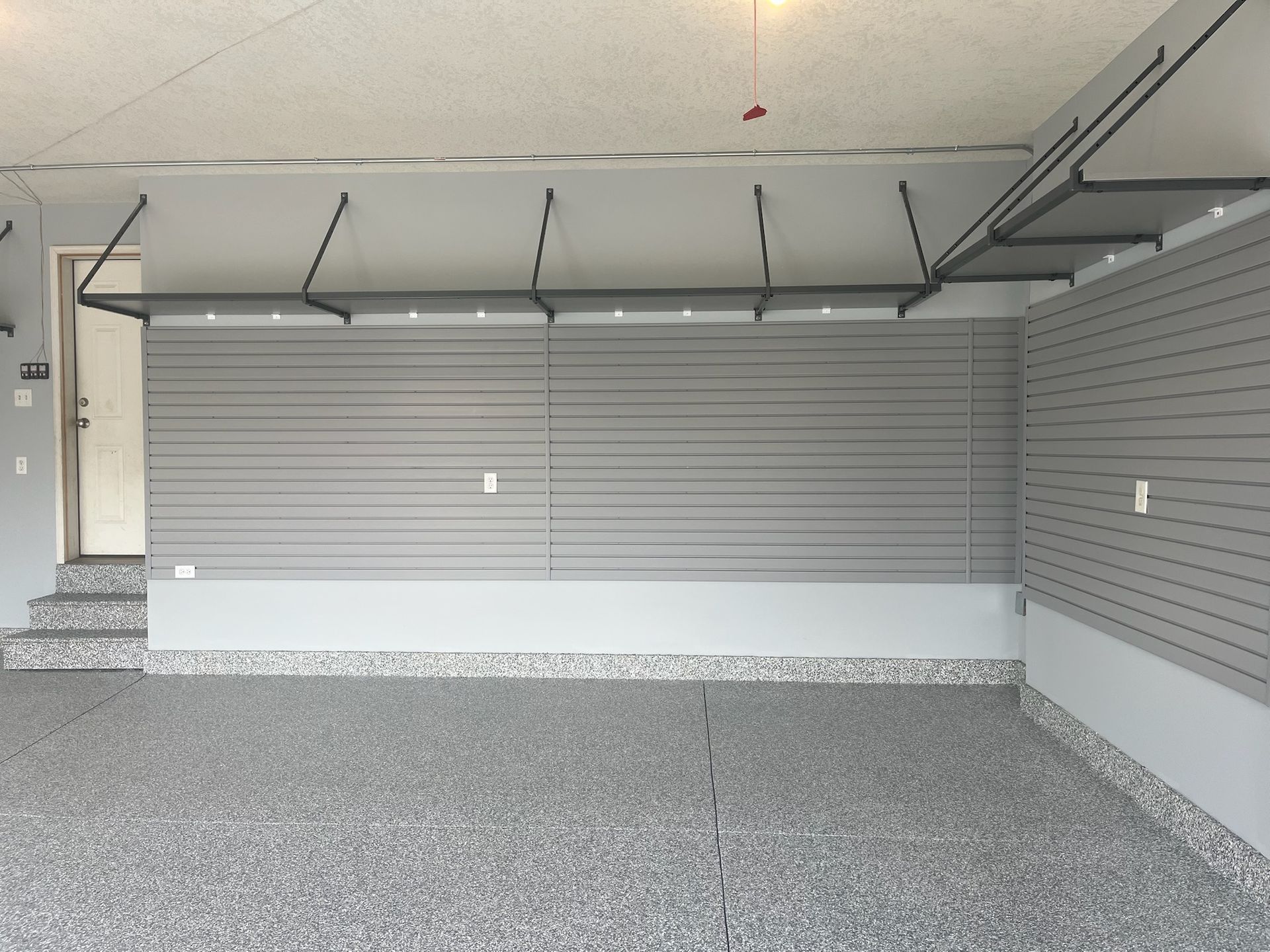 Empty garage interior with gray floor, white walls, and an open sectional door.
