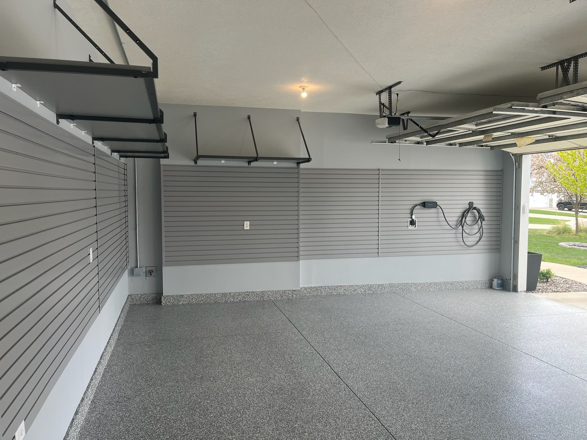 Covered garage with gray slat walls, ceiling lights, bike hooks, and a speckled concrete floor.