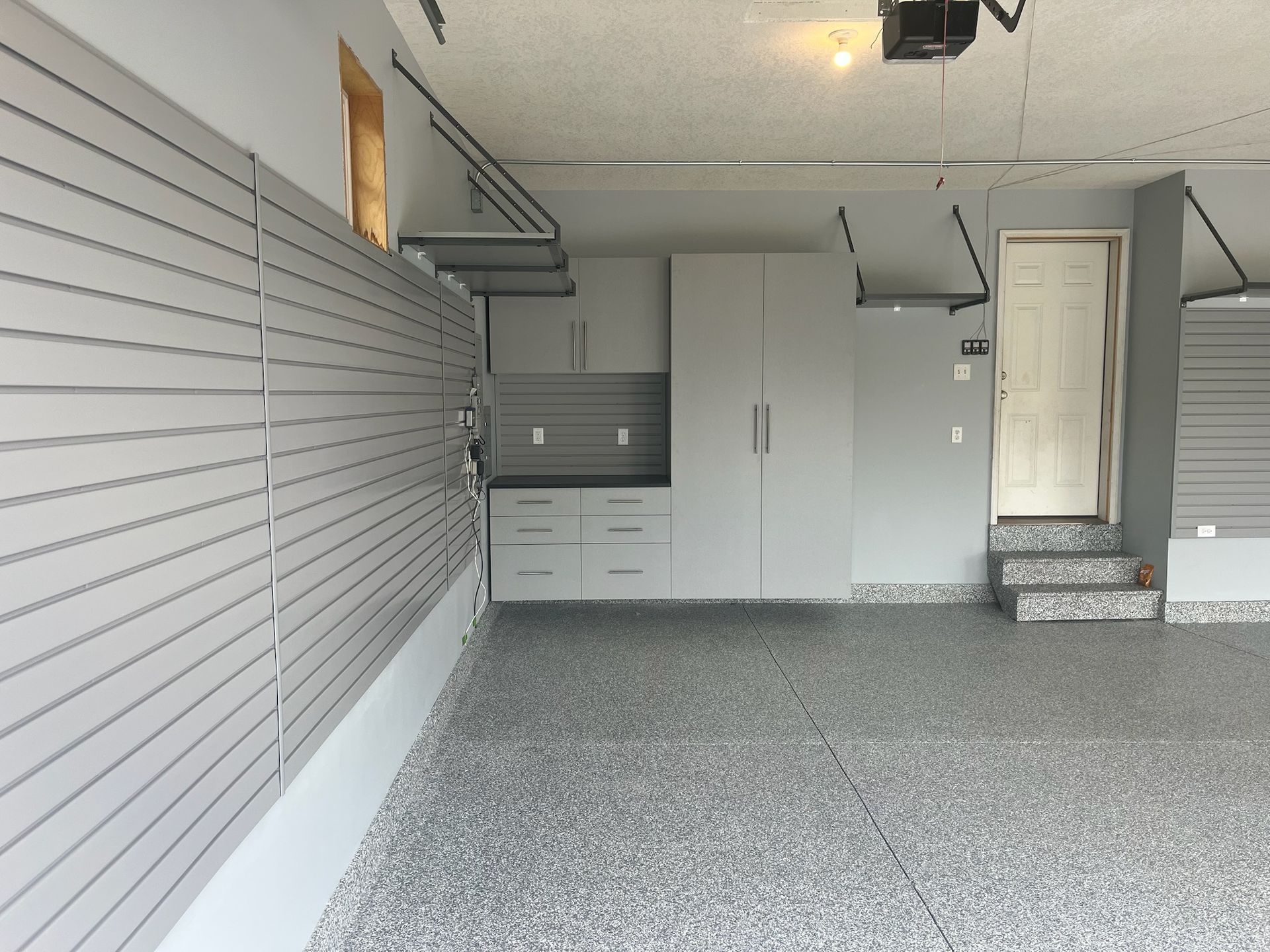 Empty garage interior with gray slat wall, cabinets, and a small carpeted step leading to a side door