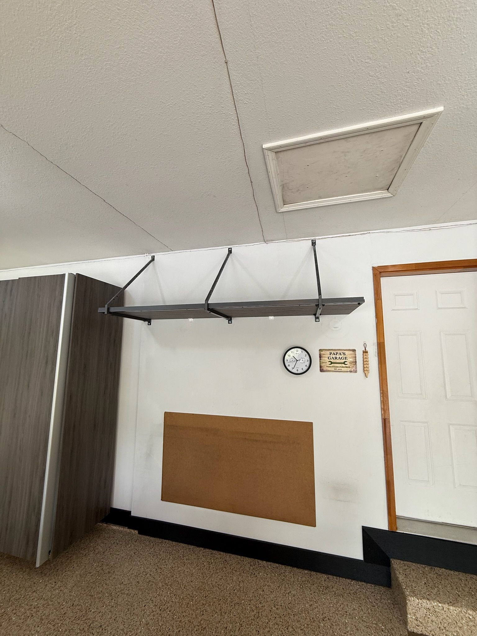 Empty indoor room with a white ceiling, wall clock, bulletin board, and a white door on the right.