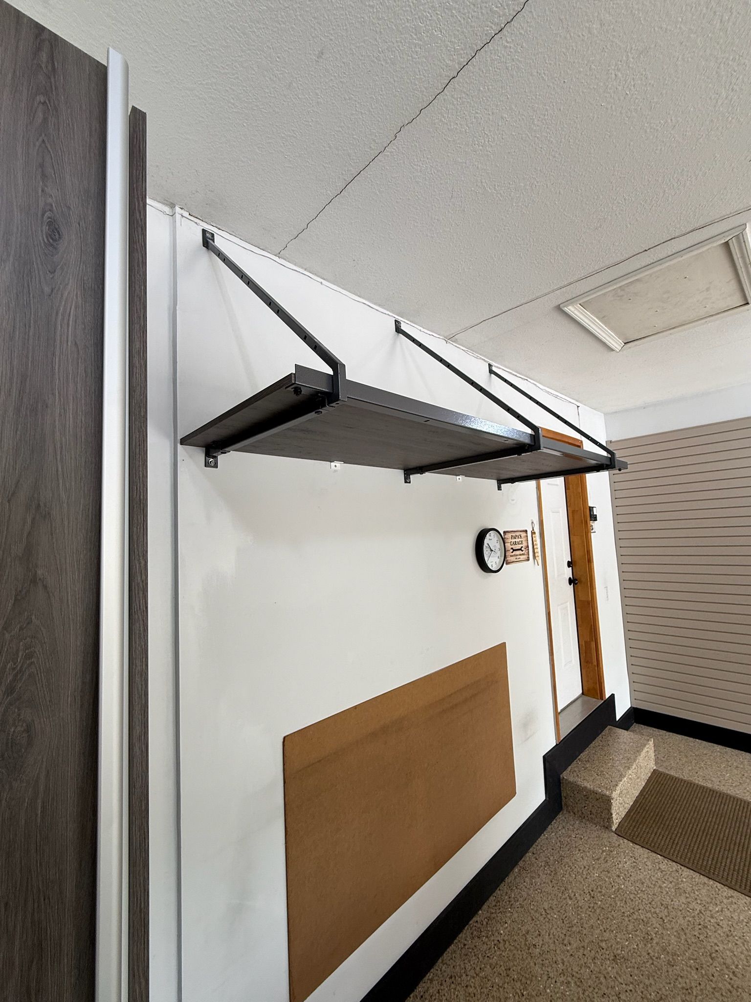 Wall-mounted folding desk shelf in a hallway, with a corkboard panel and ceiling tiles visible.