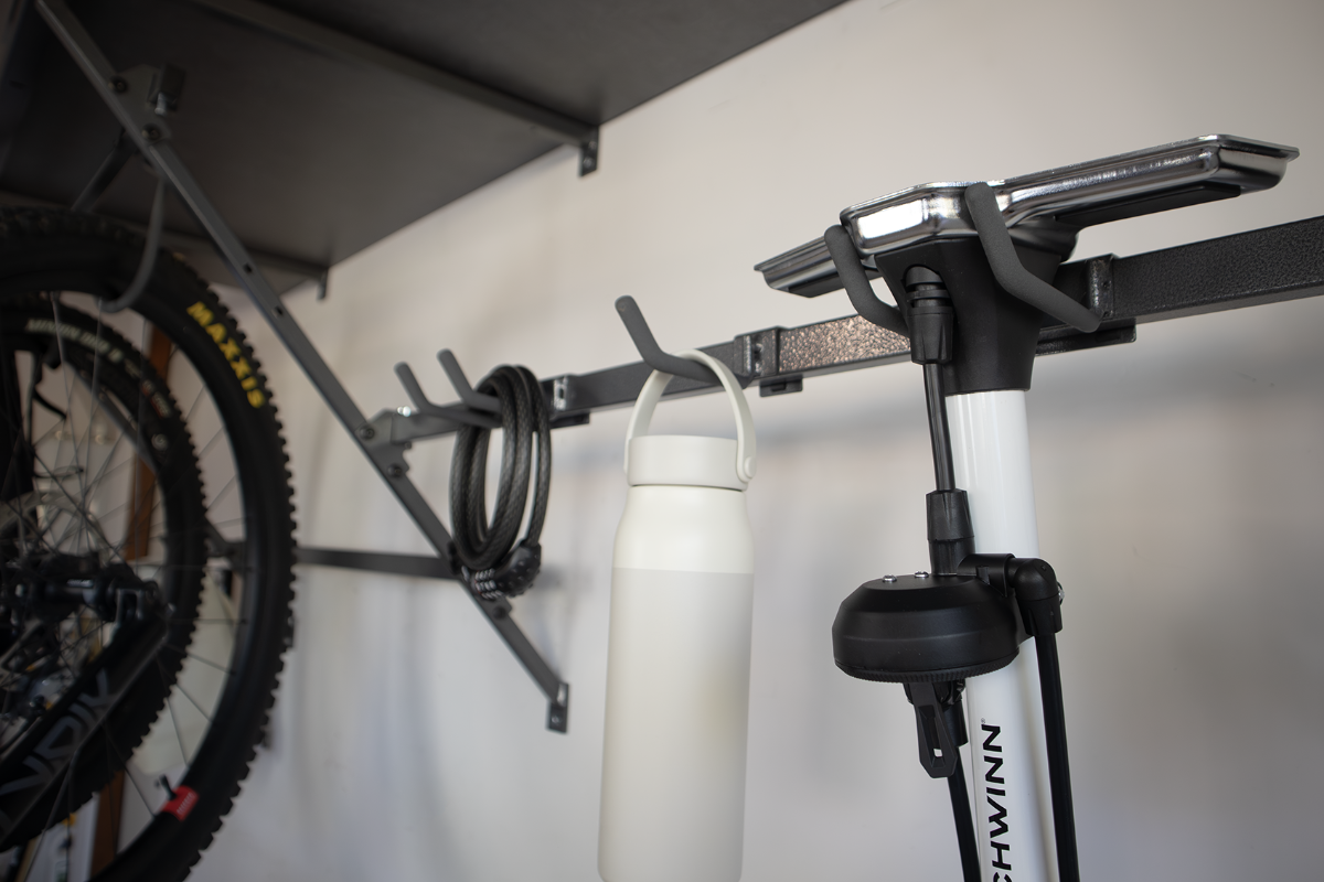 Bicycle accessories hanging on a wall-mounted rack in a garage: a water bottle, bike lock, and air pump.