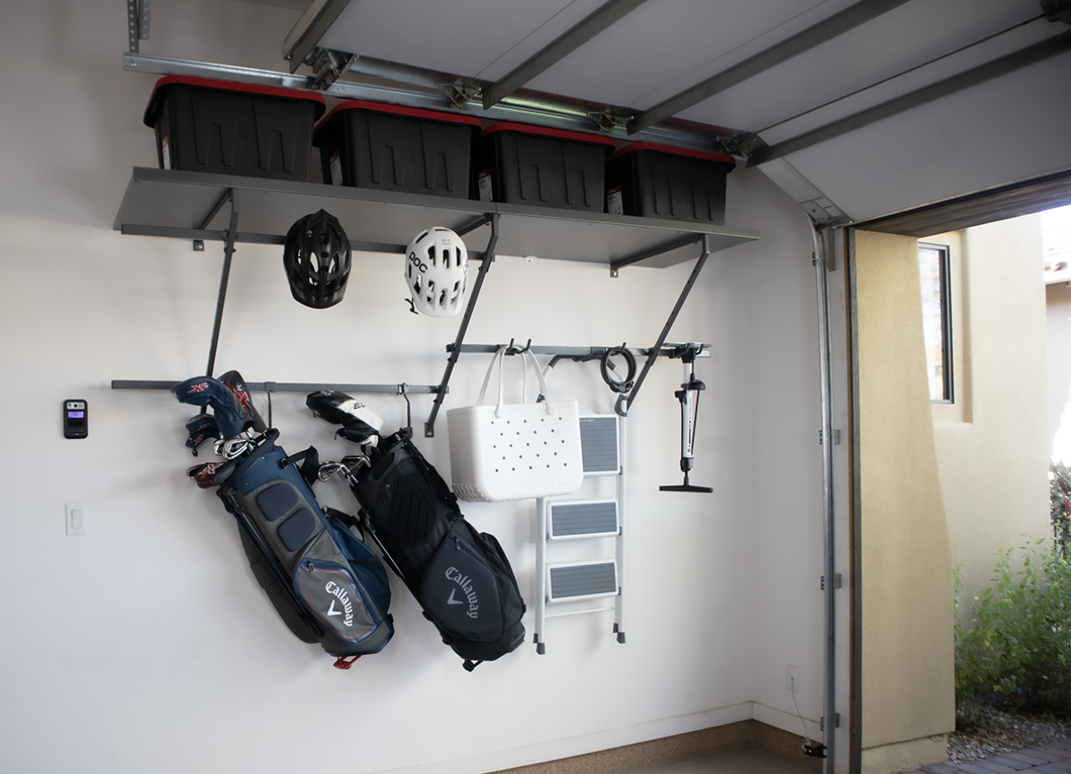 Garage storage: overhead shelf with black bins, hanging golf bags, helmets, and other equipment.