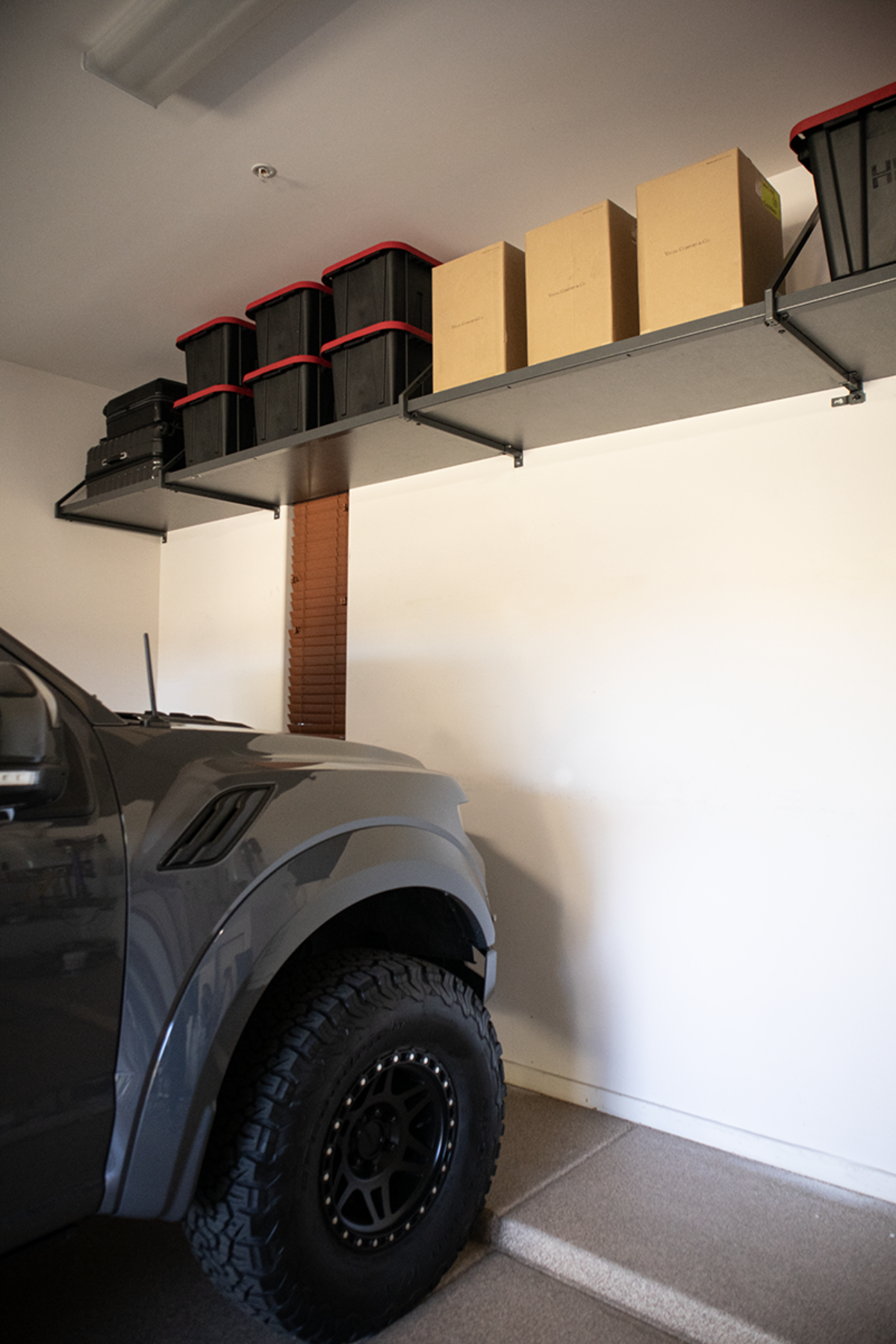 Gray truck parked in a garage with overhead shelves holding storage bins and boxes.