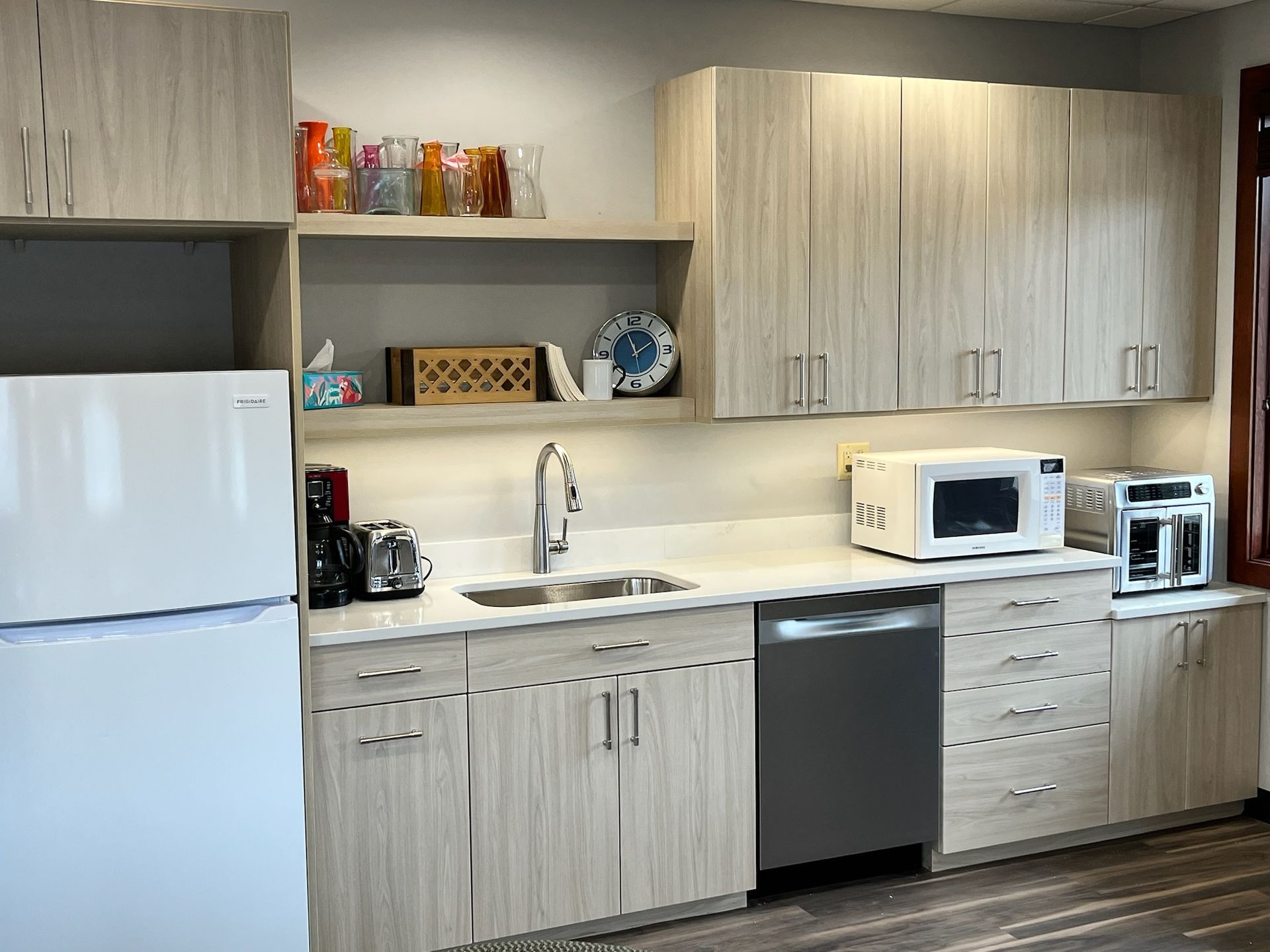 Modern kitchen with light wood cabinets, white fridge, microwave, dishwasher, and coffee maker