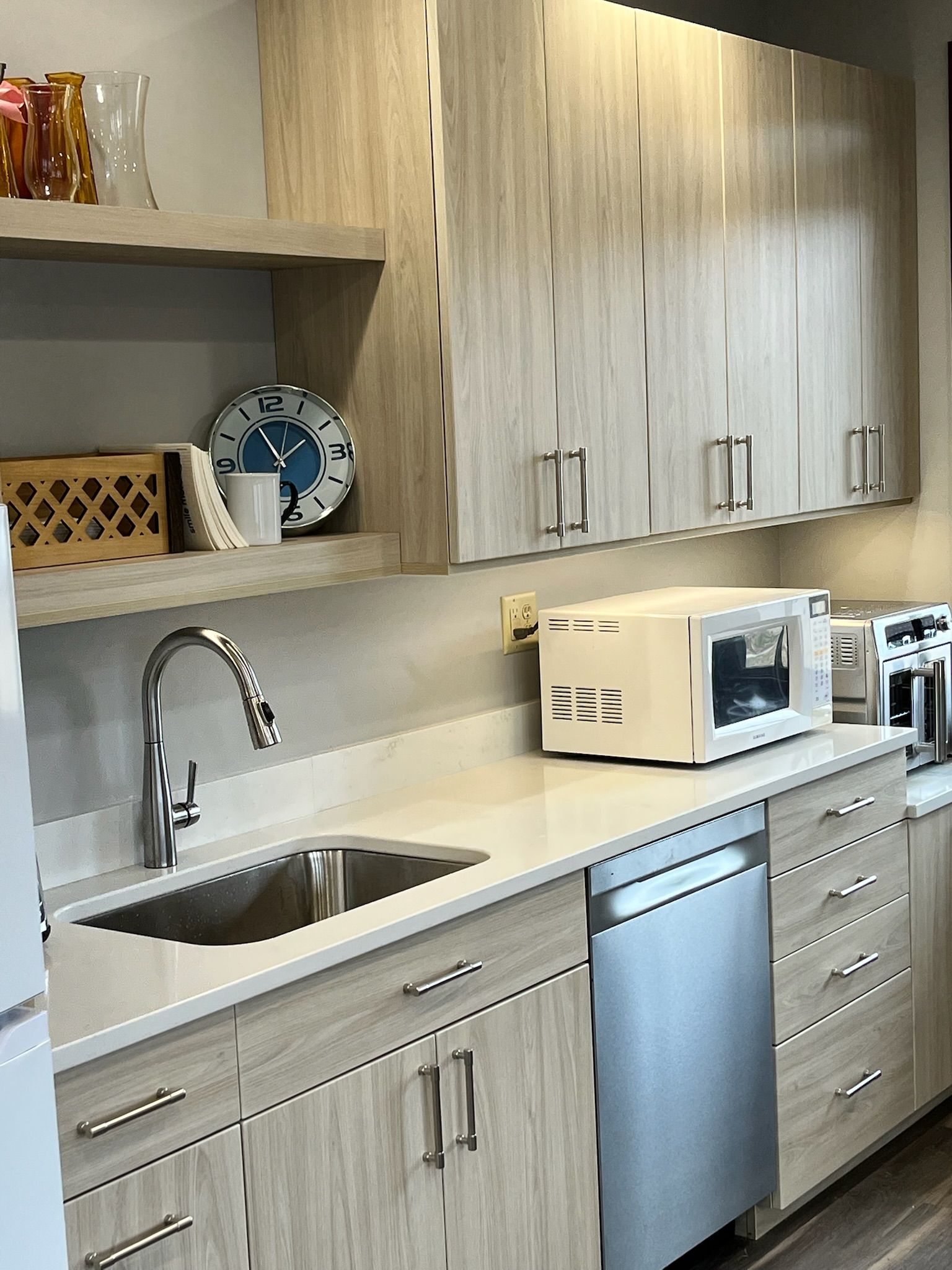 Modern kitchen with light wood cabinets, sink, microwave, and stainless-steel dishwasher and drawers