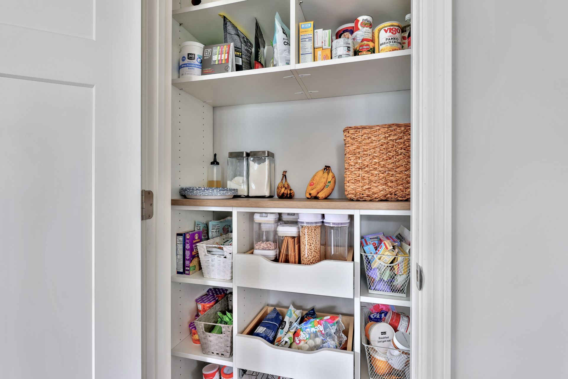 Open pantry closet with organized shelves of snacks, jars, and pantry items