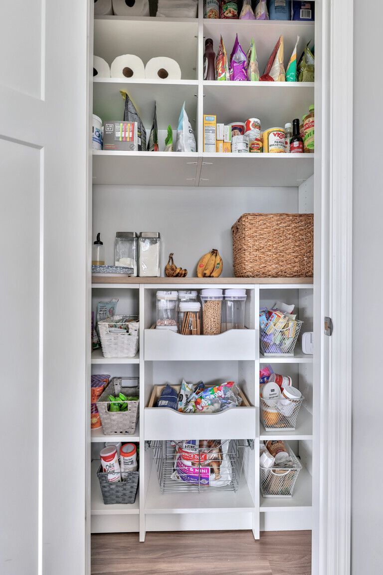 Open pantry with neatly organized craft supplies, bins, rolls, bottles, and ribbons on white shelves
