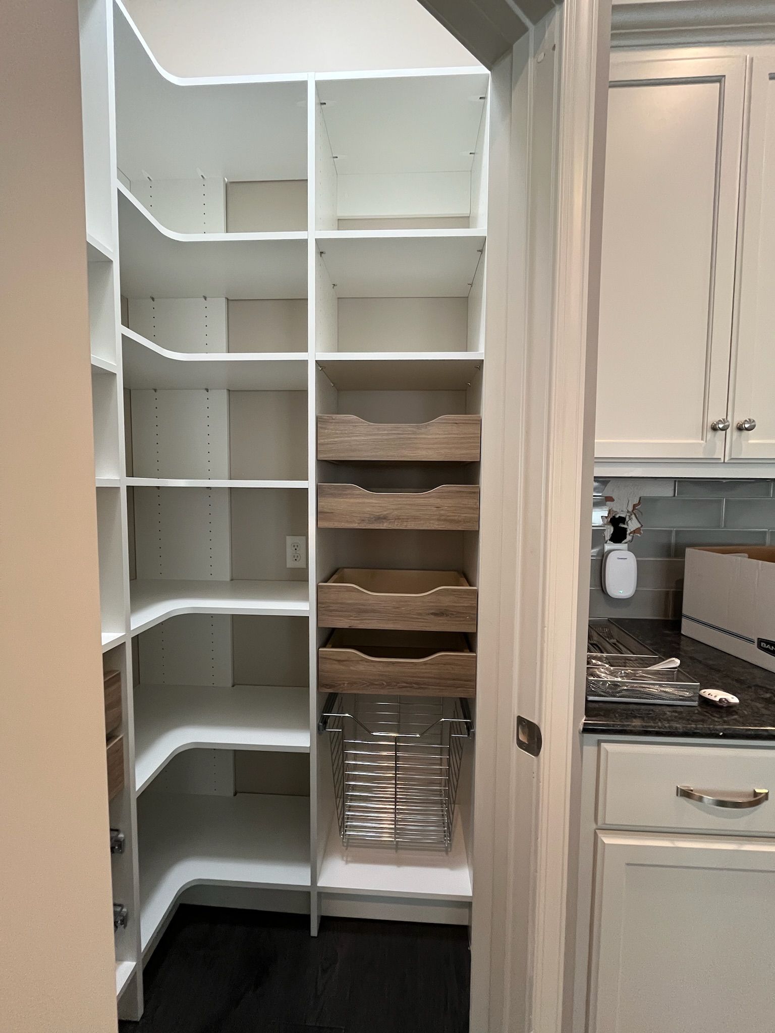 Open pantry with white shelves, wood drawers, and pull-out metal baskets beside a kitchen counter.