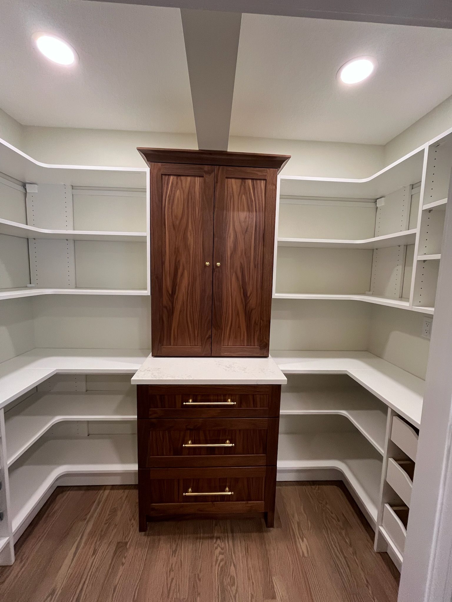 Built-in closet with white shelves, a dark wood cabinet, and a central drawer unit in a bright room