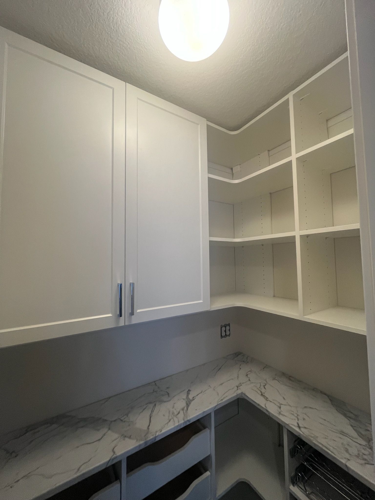 White kitchen cabinets and open corner shelving above gray countertops under a ceiling light.
