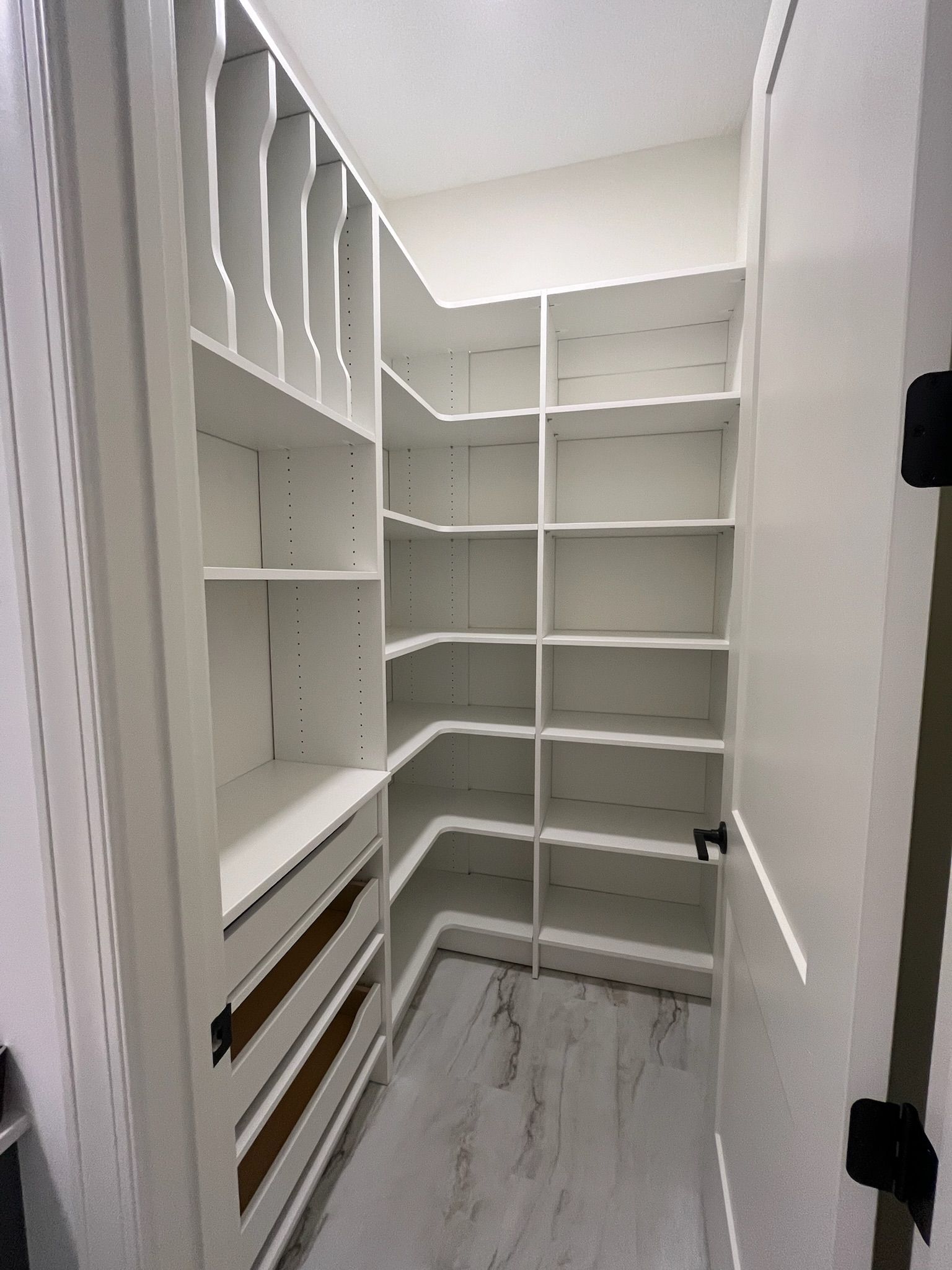 Empty white walk-in closet with built-in shelves and drawers, viewed from the doorway.
