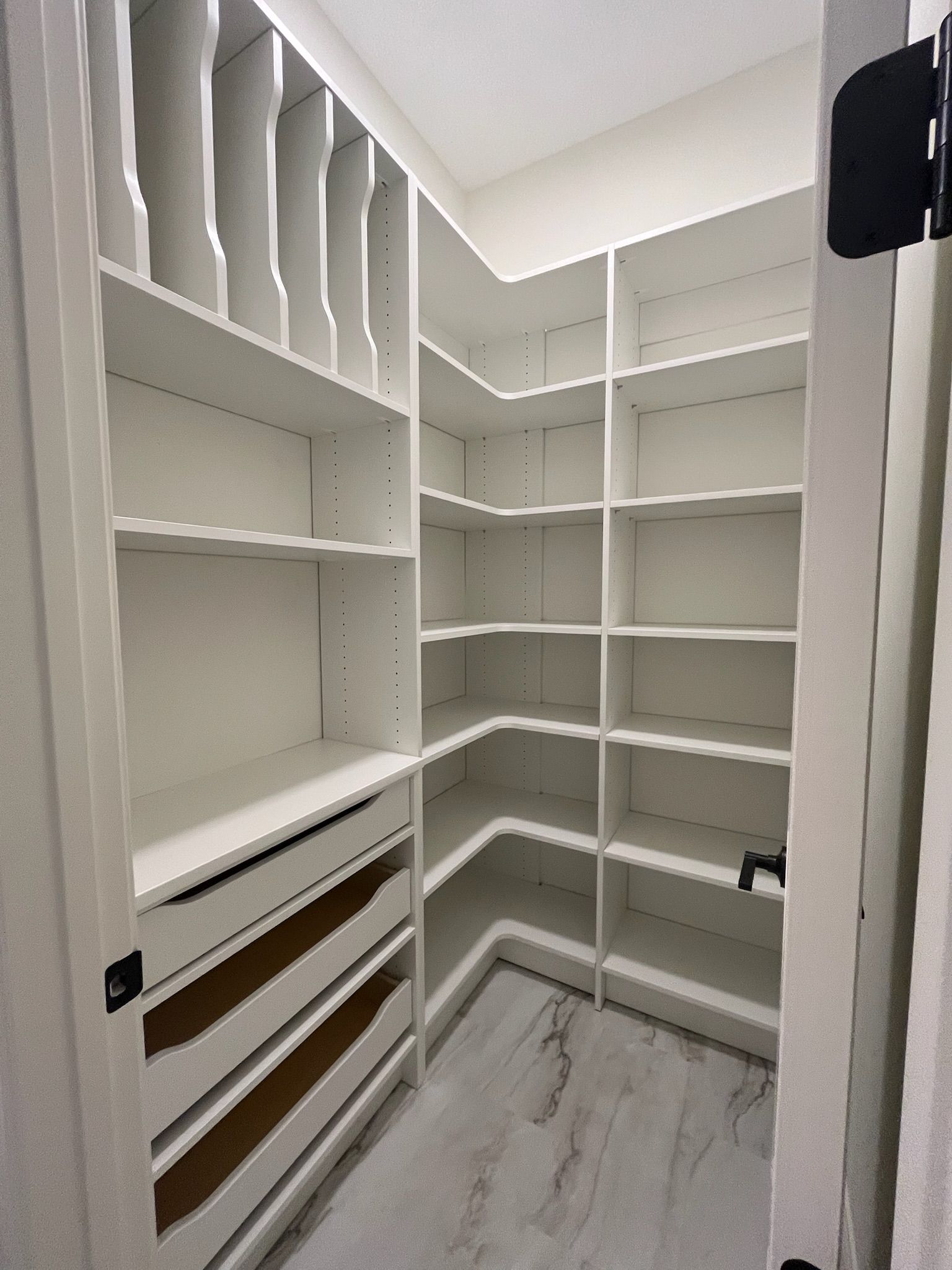 Empty white walk-in closet with built-in shelves, drawers, and hanging rods on gray flooring